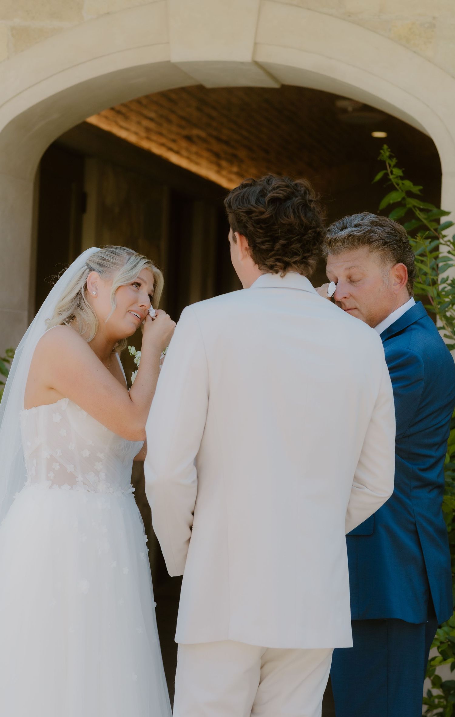 Bride and groom holding hands with officiant during intimate outdoor wedding ceremony under stone arch.