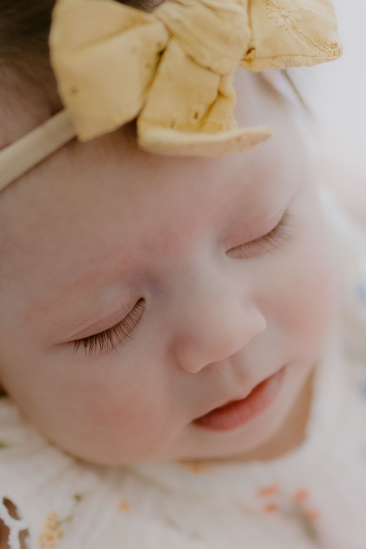 Close-up of a peacefully sleeping newborn baby wearing a yellow bow headband.