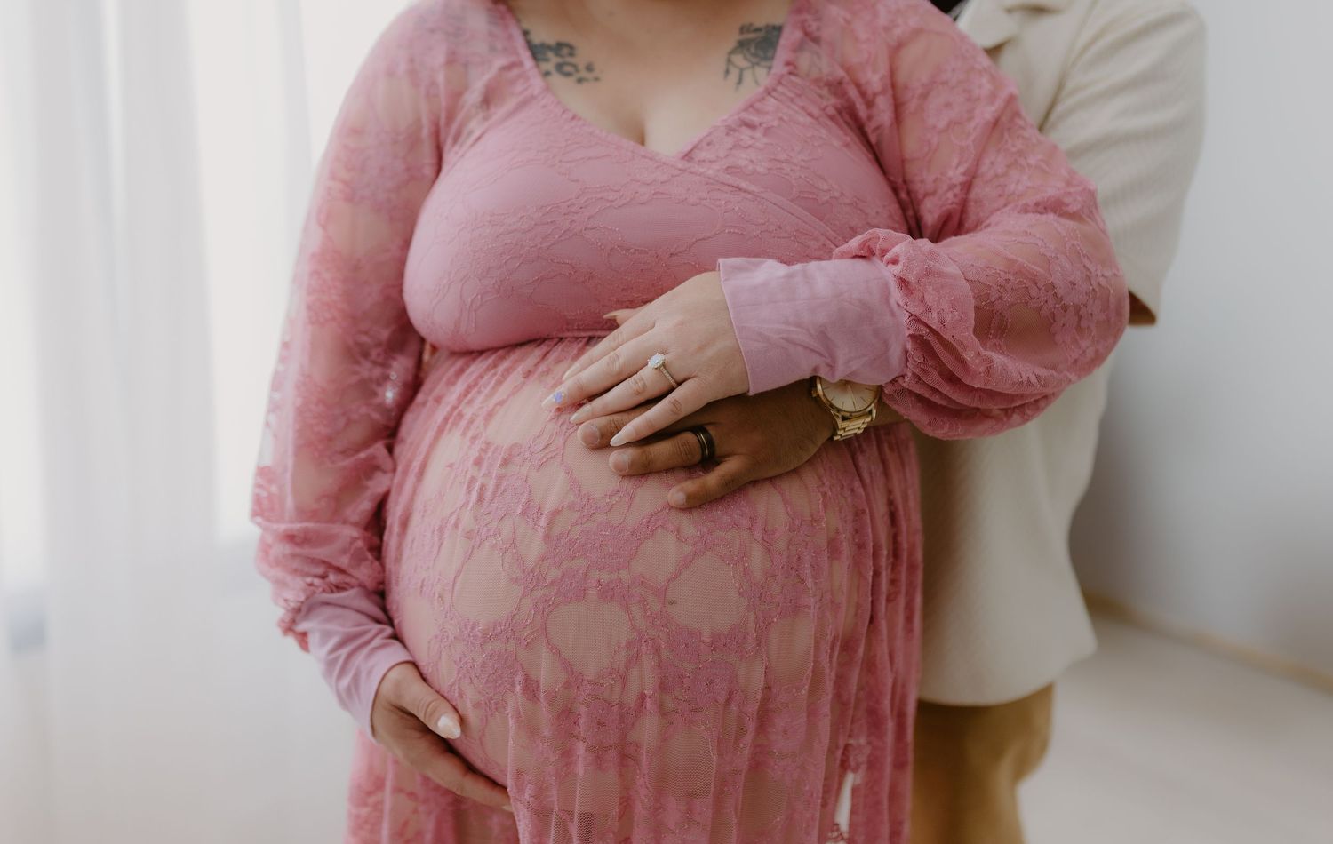 Close-up of pregnant woman in pink floral dress with partner's hands lovingly cradling her bump.