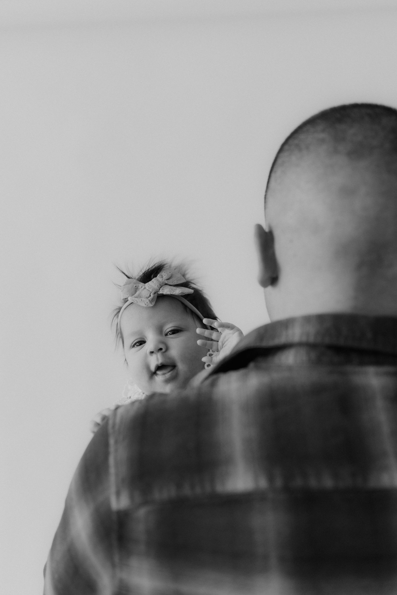 Black and white photo of a bald father holding his smiling baby girl wearing a bow headband.