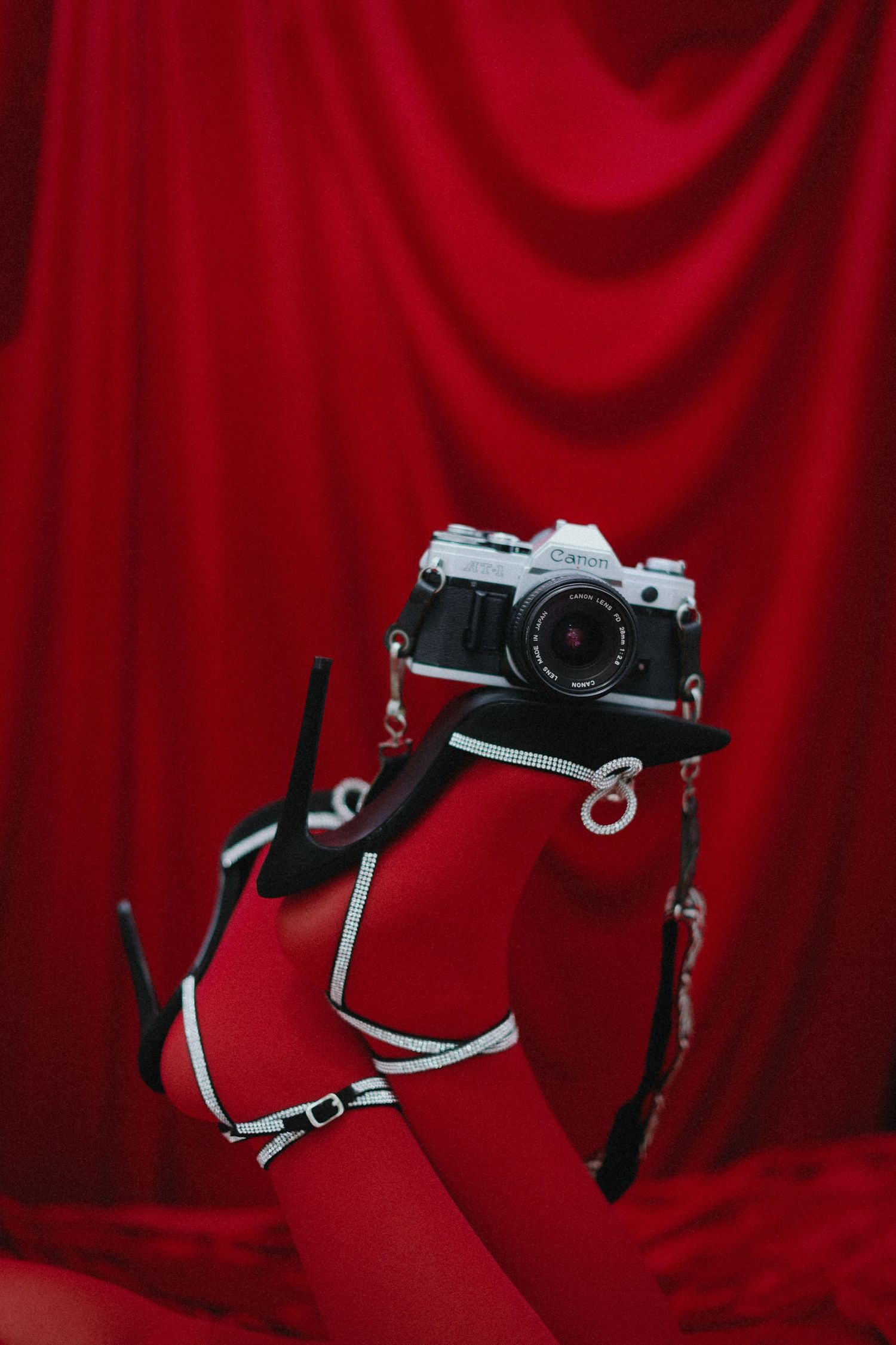 Hand holding vintage Canon film camera against dramatic red velvet curtain backdrop.