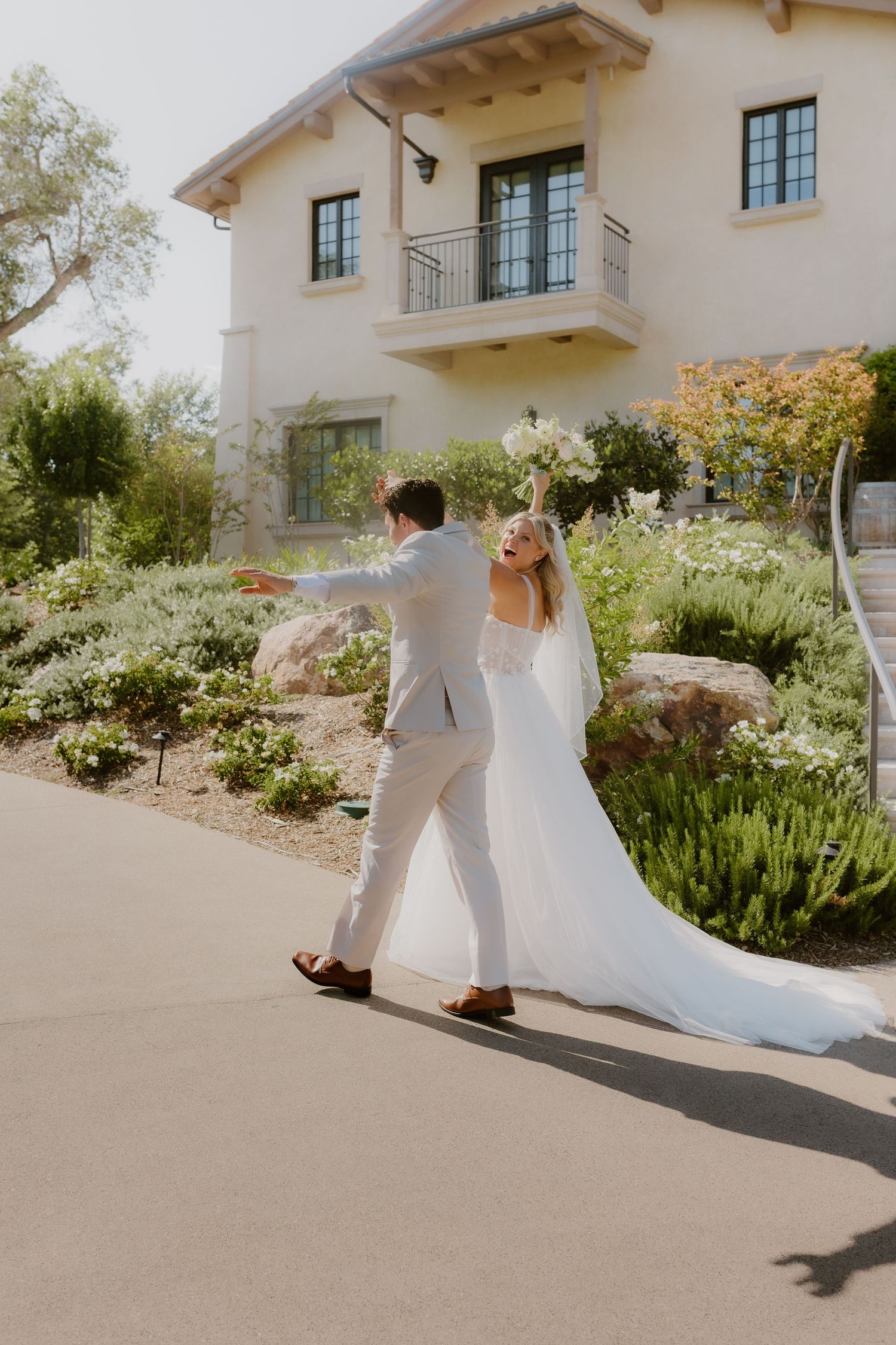 Bride and groom dancing joyfully outside an elegant venue, bride holding bouquet aloft in white gown. Wedding, Candid