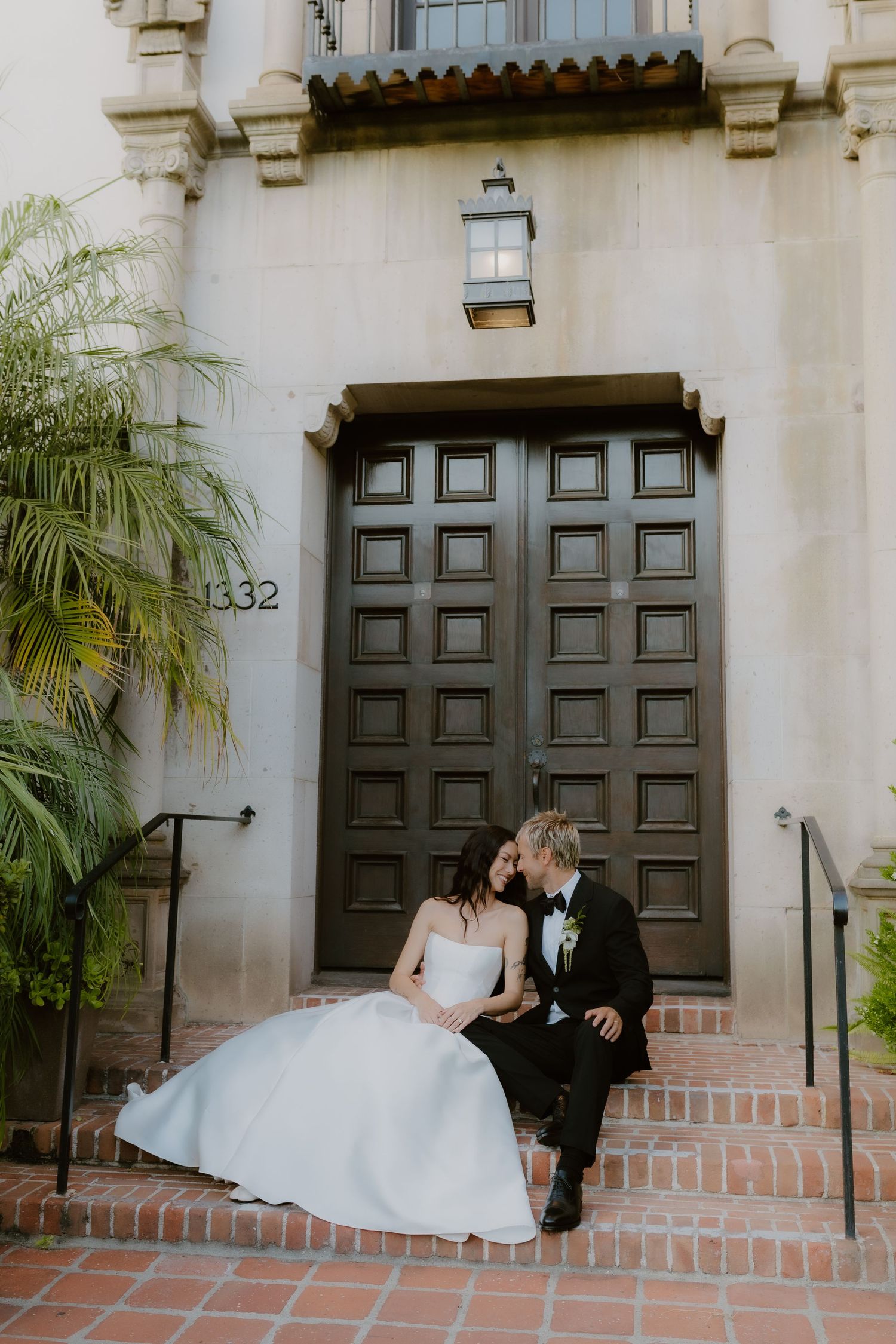 Bride in white gown and groom in black tux share a romantic kiss on brick steps at address 1332.