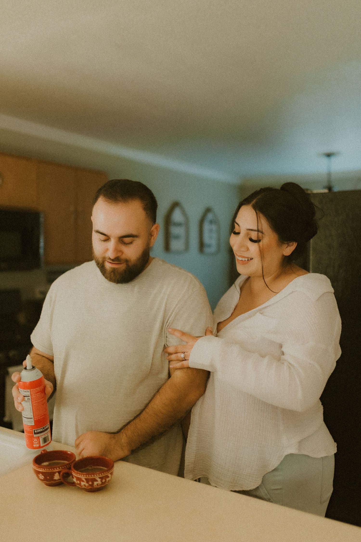 Couple shares a lighthearted moment preparing hot drinks with whipped cream in a cozy home kitchen.