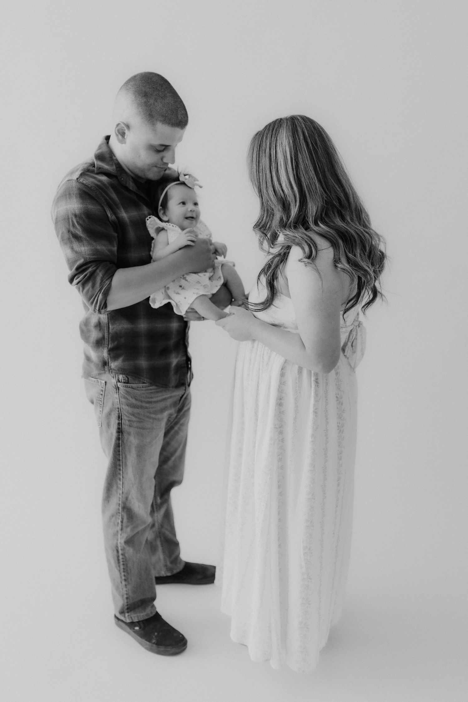 Black and white family portrait of a man and woman in a studio lovingly attending to their baby girl.