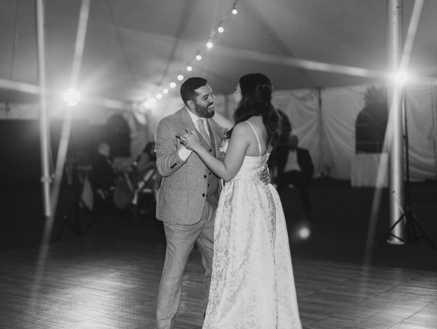 Black and white romantic first dance photo of bride and groom under soft reception lighting.