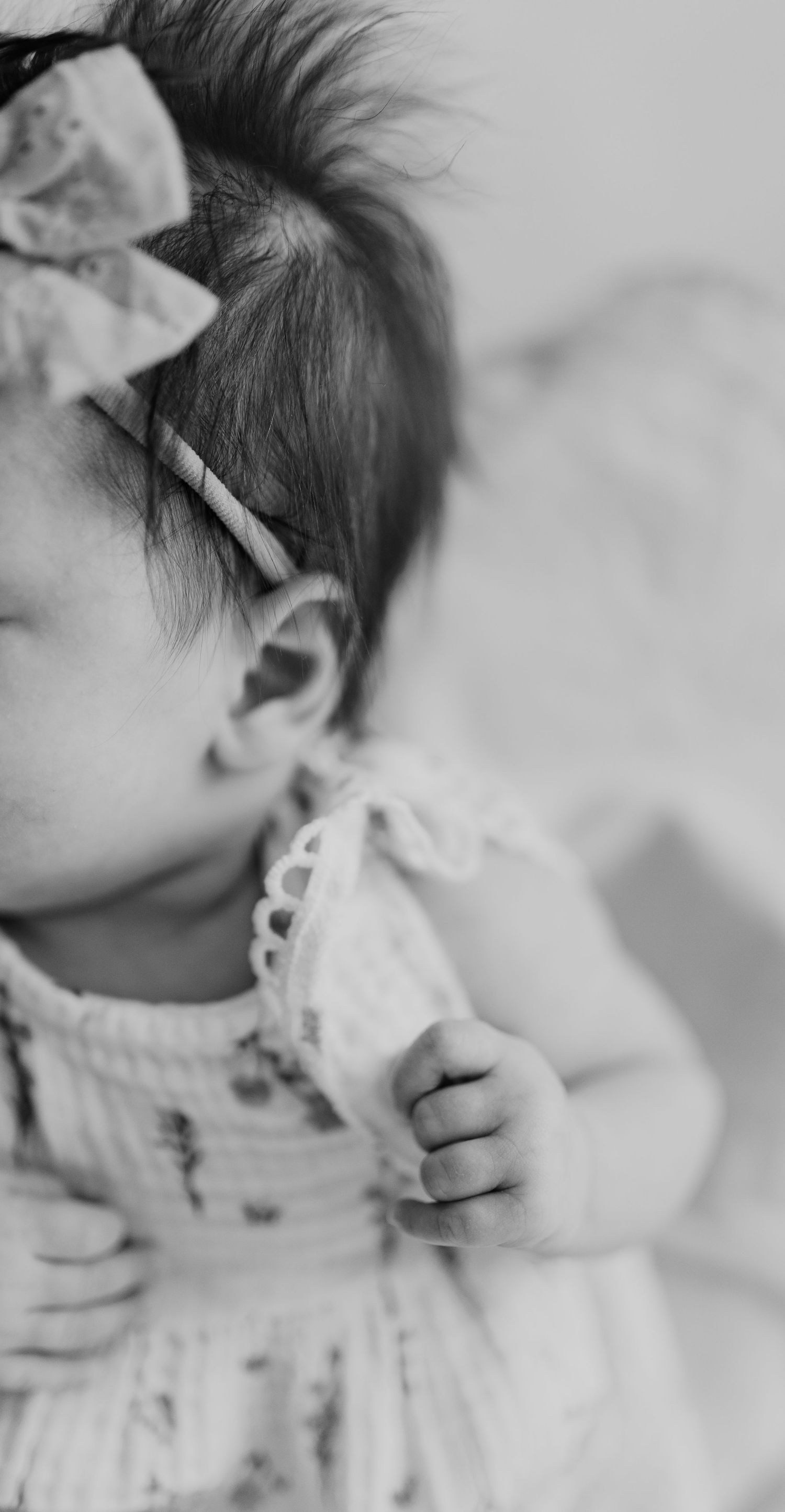 Black and white close-up of a newborn baby girl wearing a bow headband and floral dress.