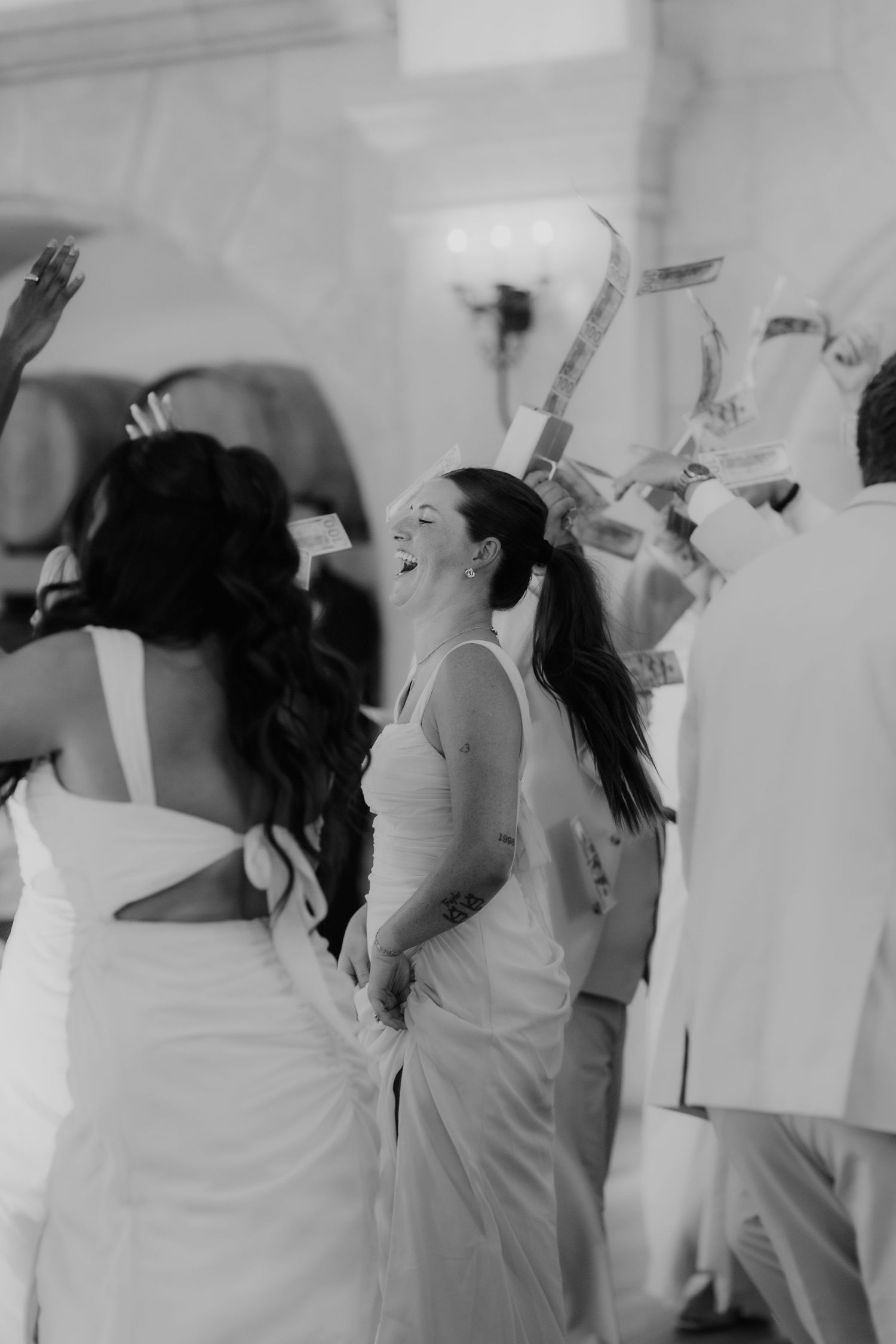 Black and white photo of joyful bride laughing during lively wedding reception dance celebration.