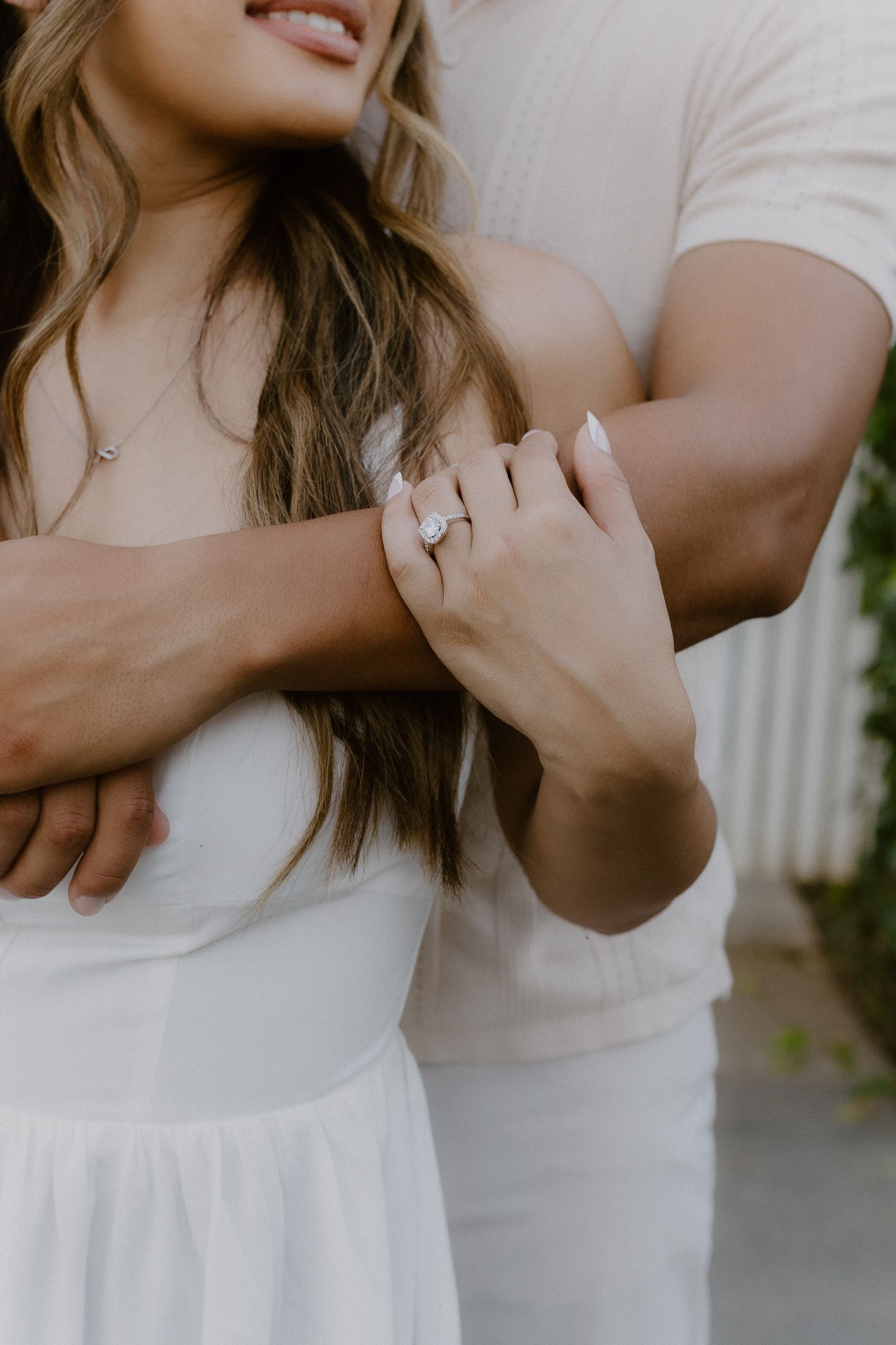 Close-up of a couple embracing, highlighting a stunning oval diamond engagement ring on her finger.