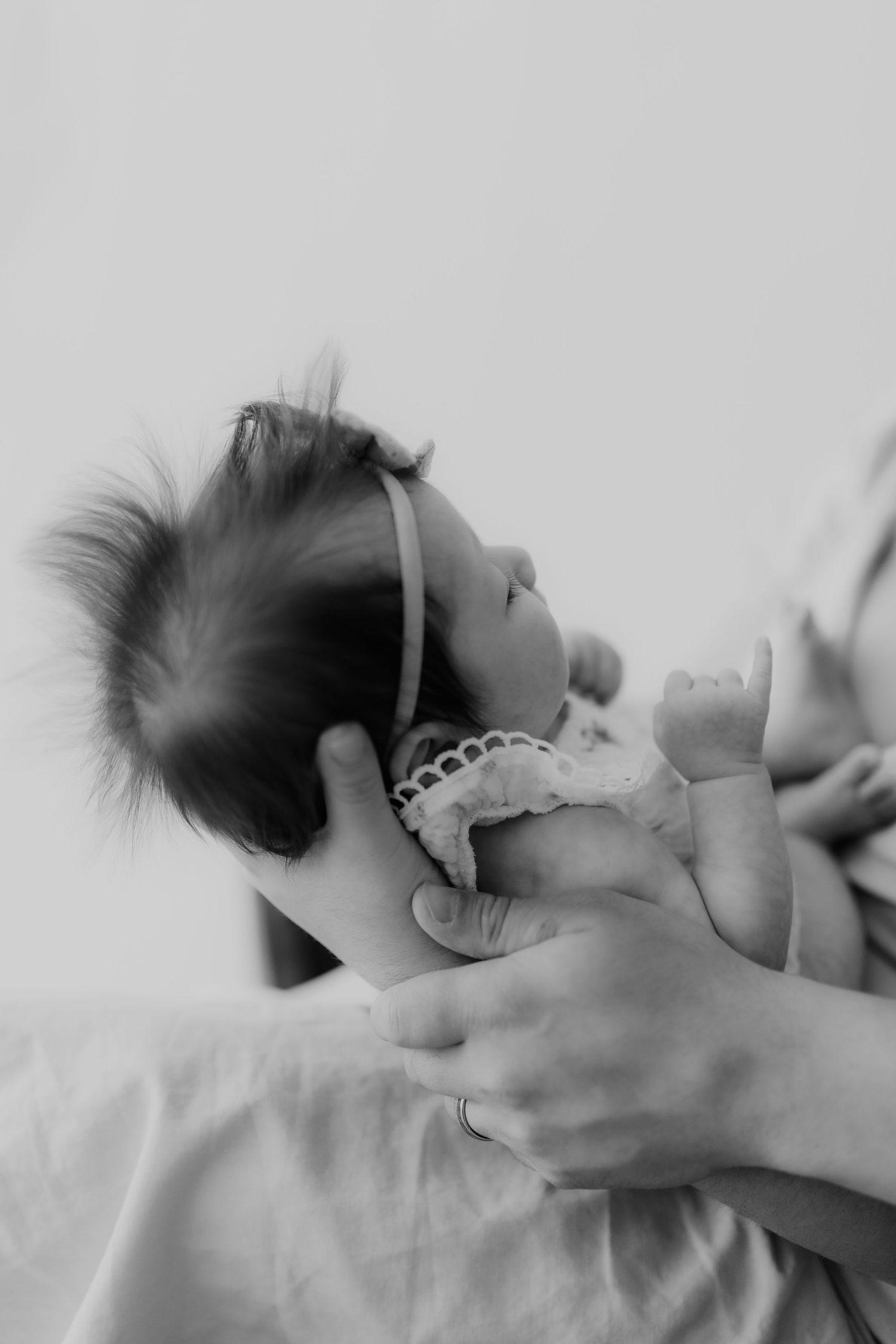 Close-up black and white photo of a newborn baby with dark hair being gently held.