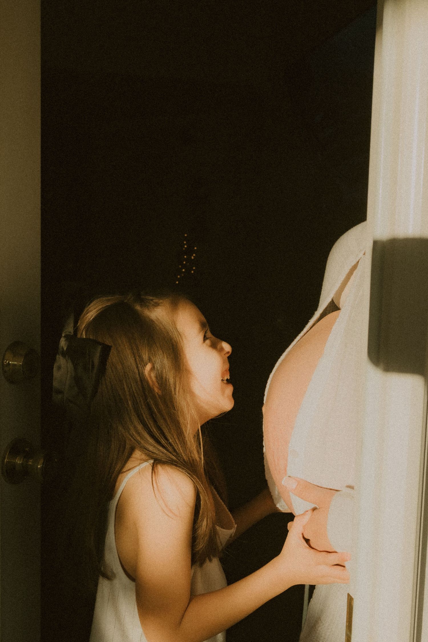 Excited young girl touching and admiring pregnant mother's bare belly in warm light.