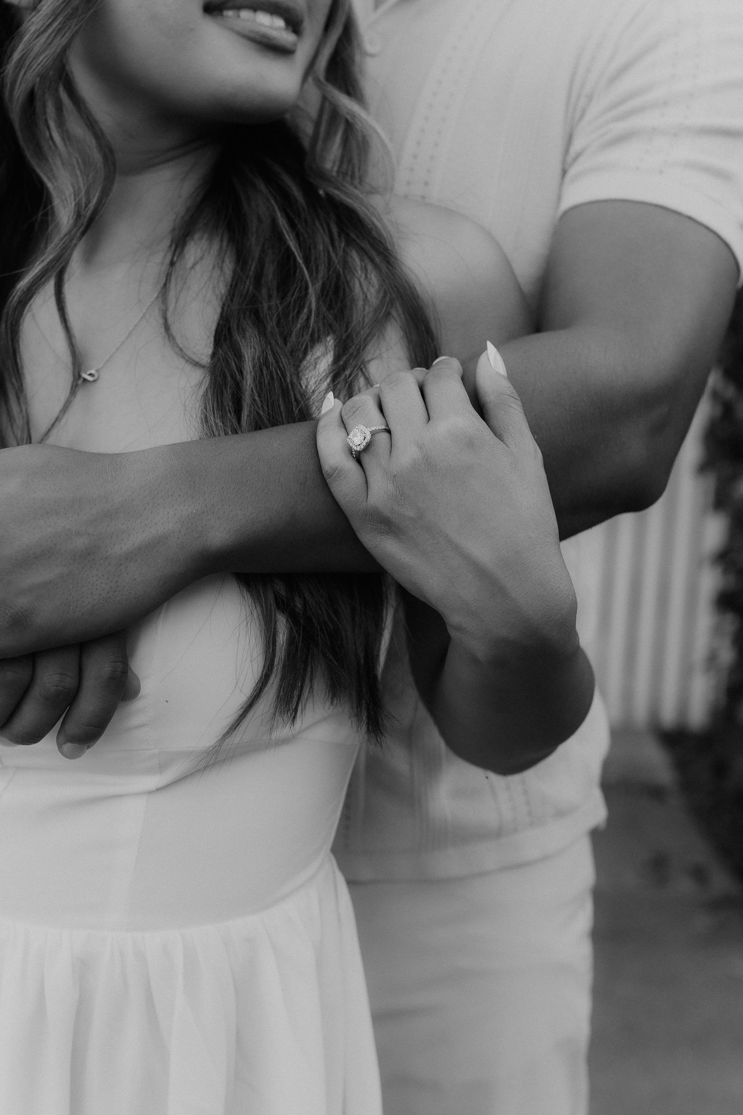 Black and white close-up of an engaged couple embracing, showcasing a sparkling oval engagement ring.