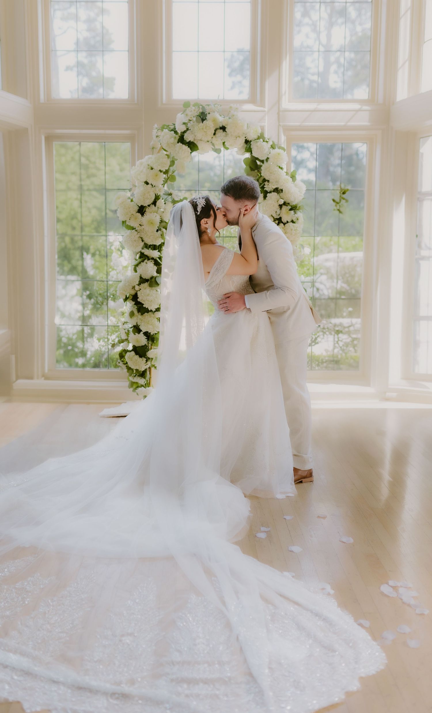 Bride and groom sharing first kiss under white floral arch in bright sunlit wedding ceremony venue. cinematic, Kohl Mansion, Burlingame