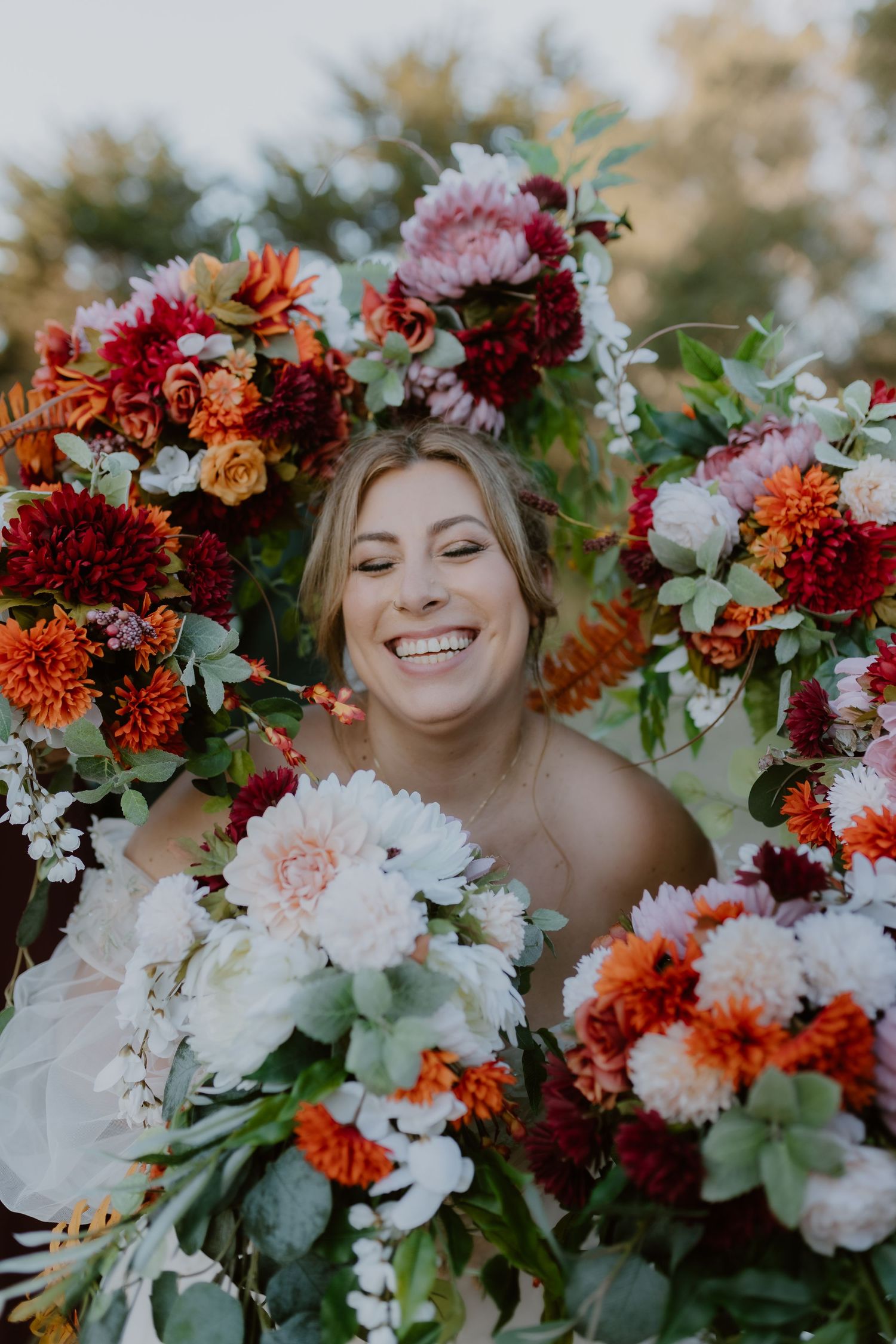 Smiling bride surrounded by vibrant red, orange, and white wedding bouquets.