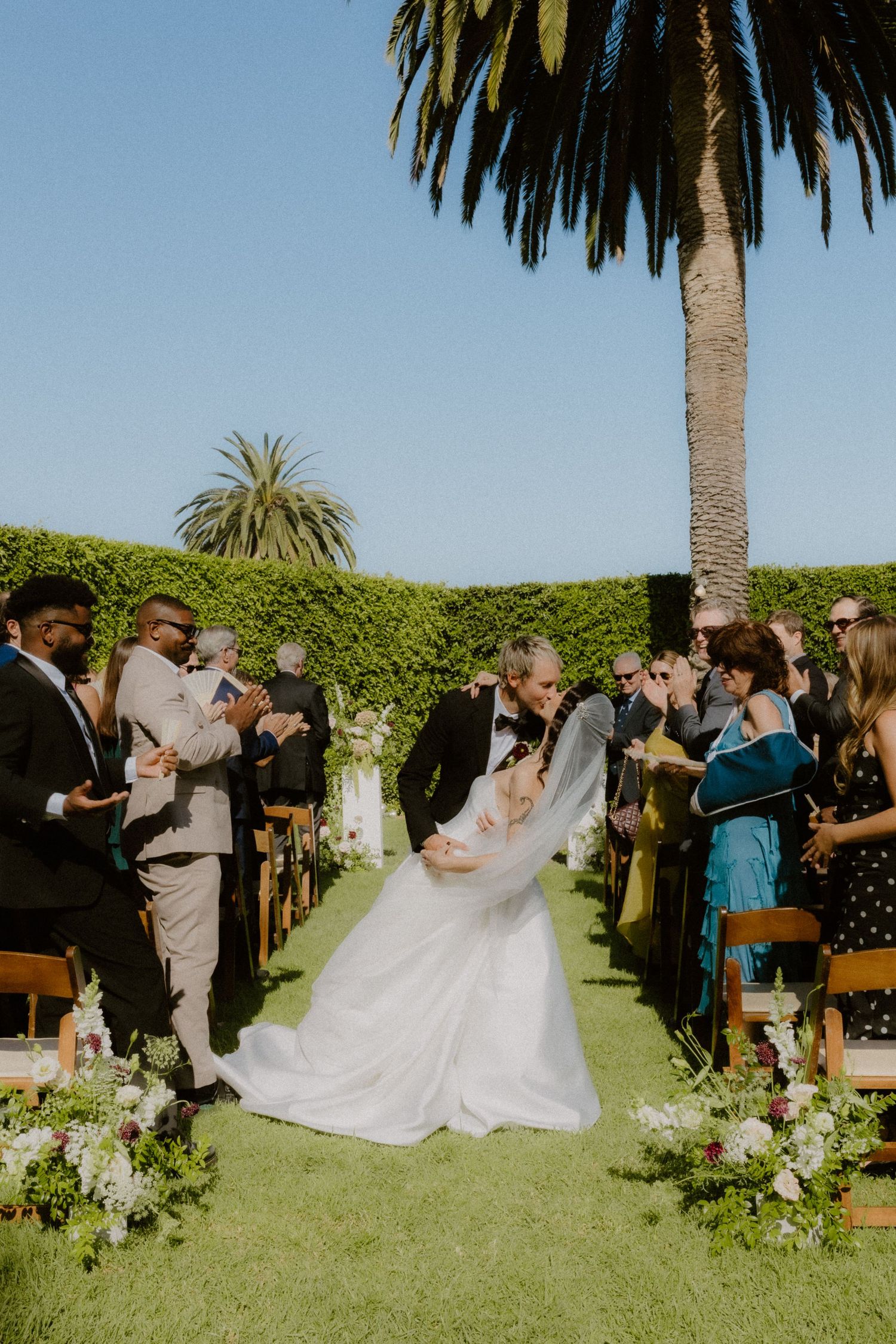 Groom dips bride for a romantic kiss during outdoor wedding recessional as guests celebrate around them.