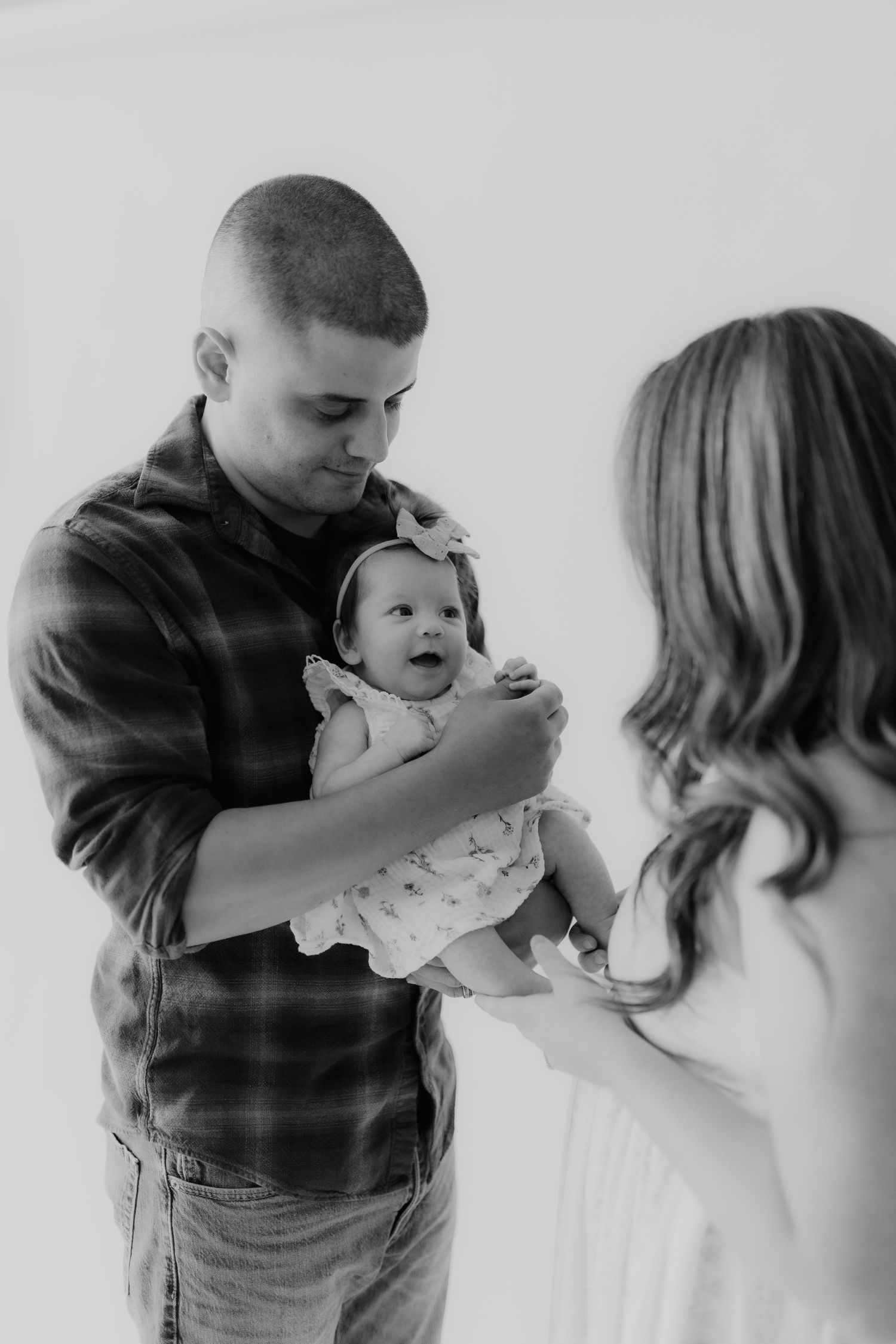 Black and white photo of a father holding his smiling newborn baby girl while mother looks on tenderly.