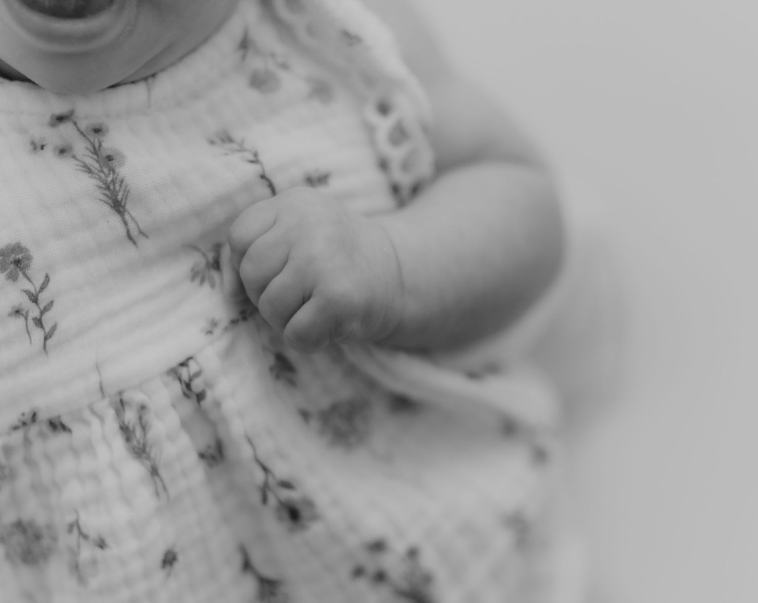 Black and white close-up of newborn baby hands in a floral muslin dress.