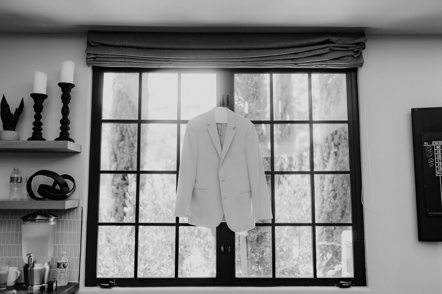 Black and white photo of white suit jacket hanging in window before wedding ceremony. monserate Winery California