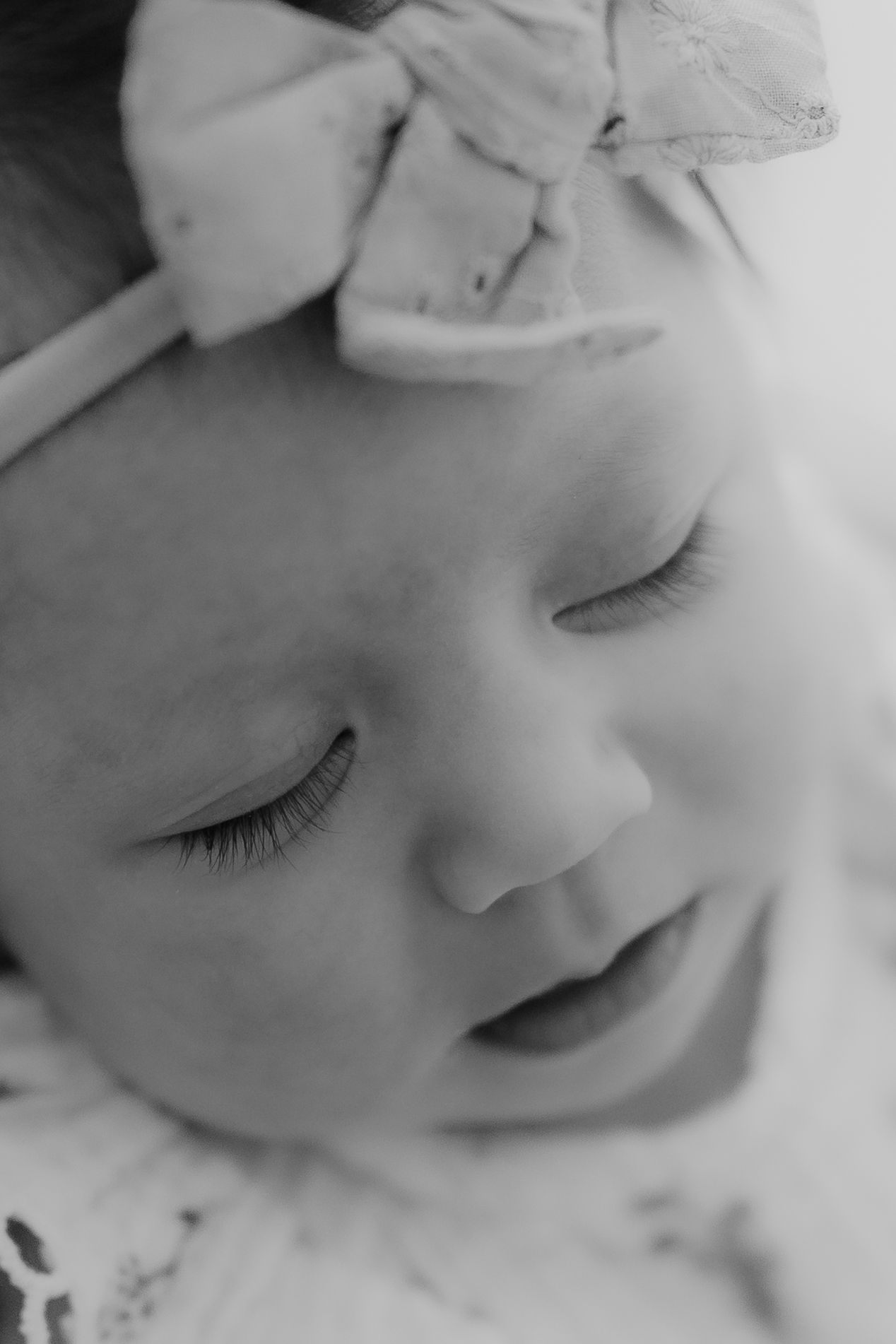Black and white close-up of a sleeping newborn baby wearing a bow headband.