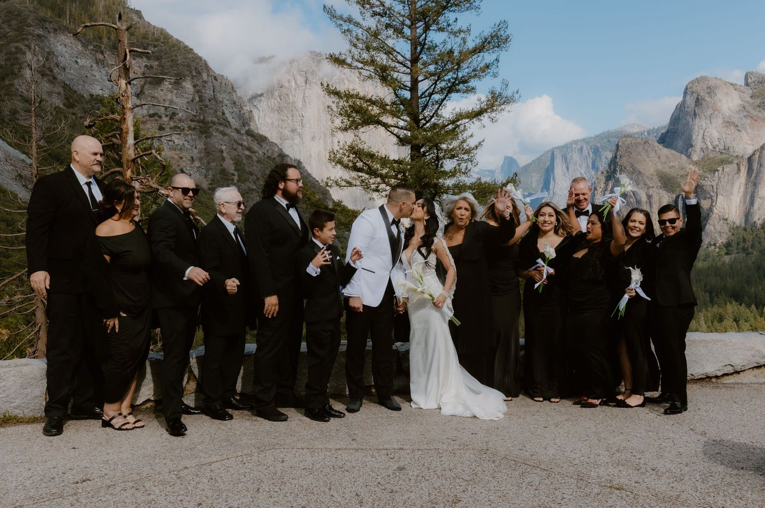 Wedding party in black attire celebrates with bride and groom against Yosemite Valley mountain backdrop. Yosemite Photographer