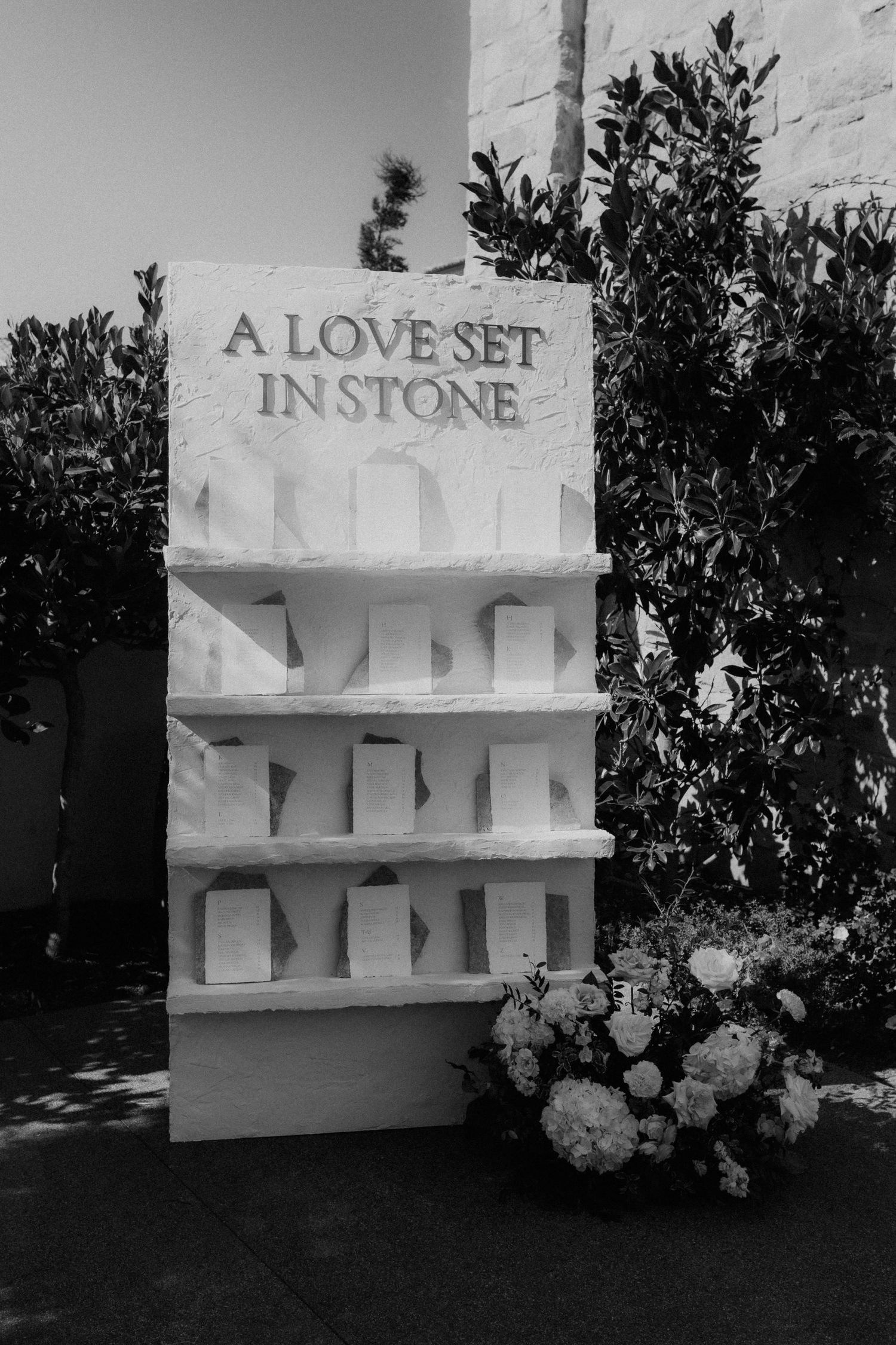 Black and white wedding seating chart display reading A Love Set In Stone with floral arrangement. Monserate Winery California