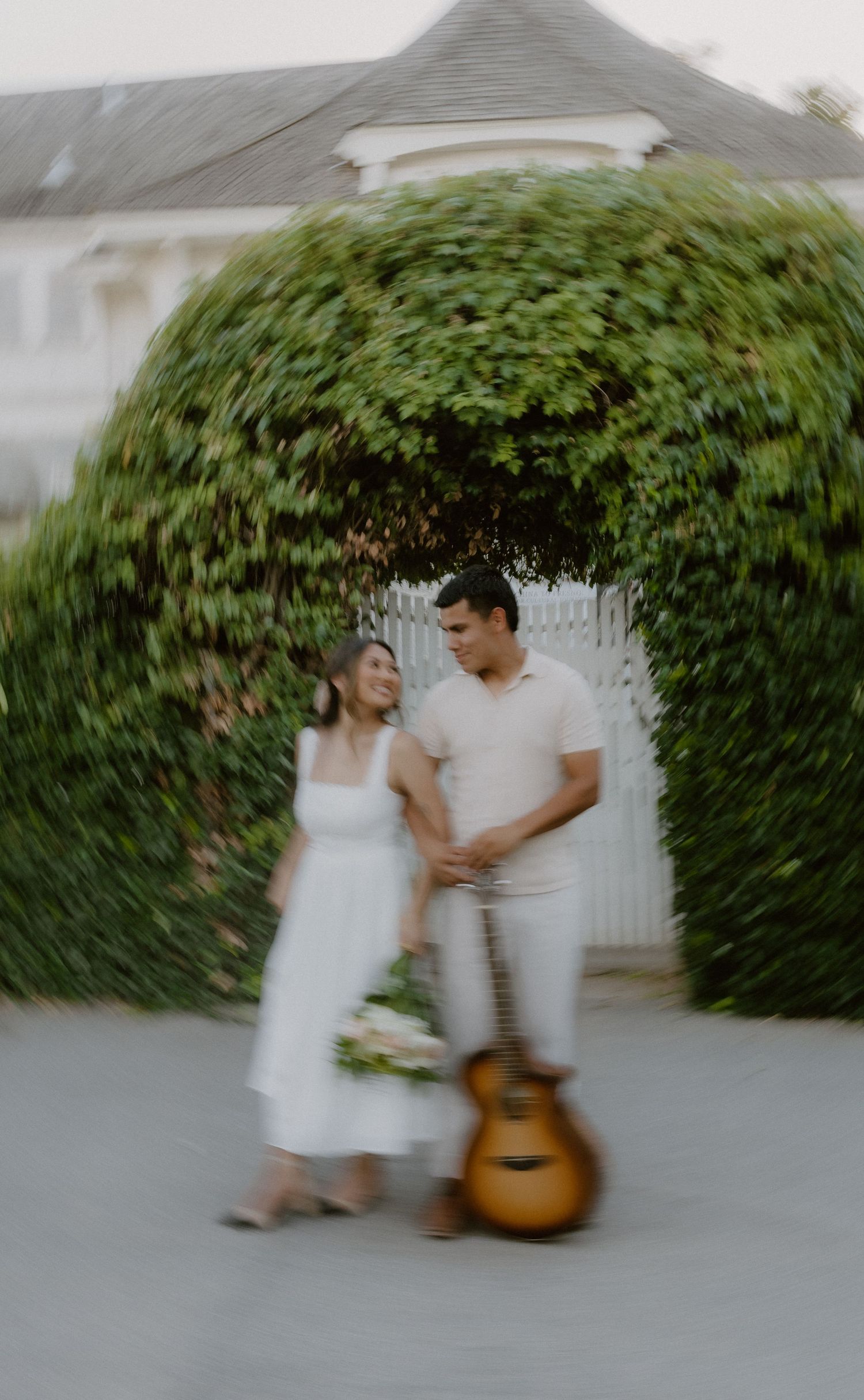 Couple holding hands beside a guitar under an ivy-covered archway at a charming estate.