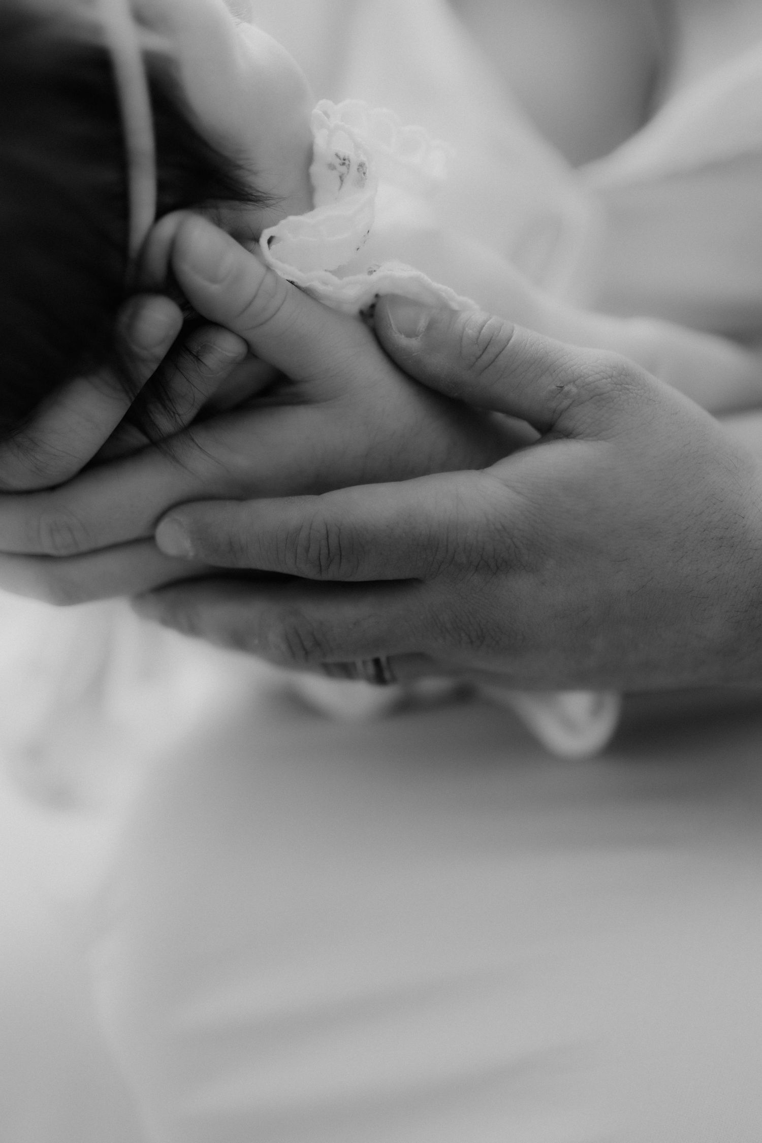 Black and white close-up of parent hands gently cradling newborn baby's head with medical tube.