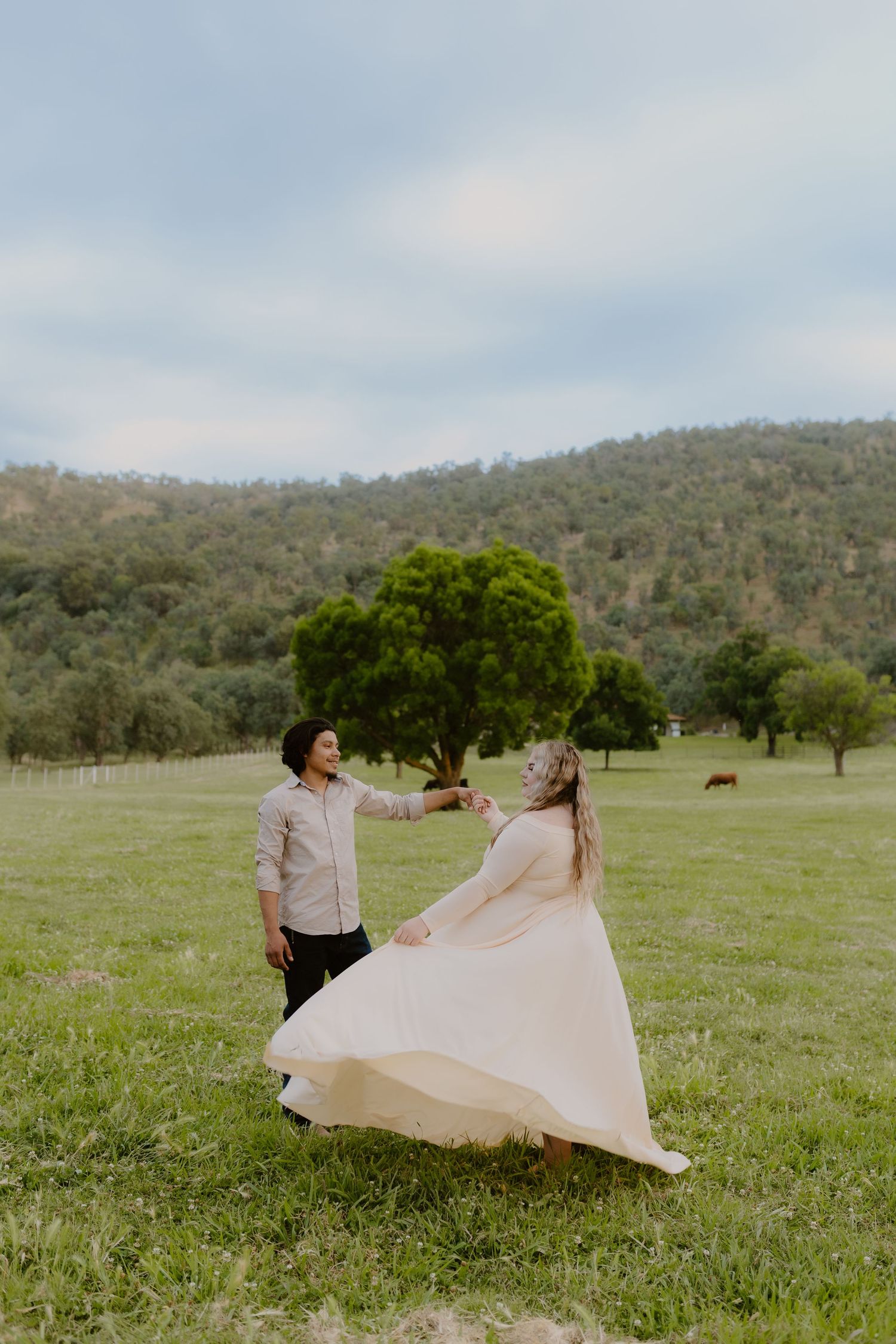 Couple dancing joyfully in a green meadow during an outdoor maternity photo session. prompted, california, maternity