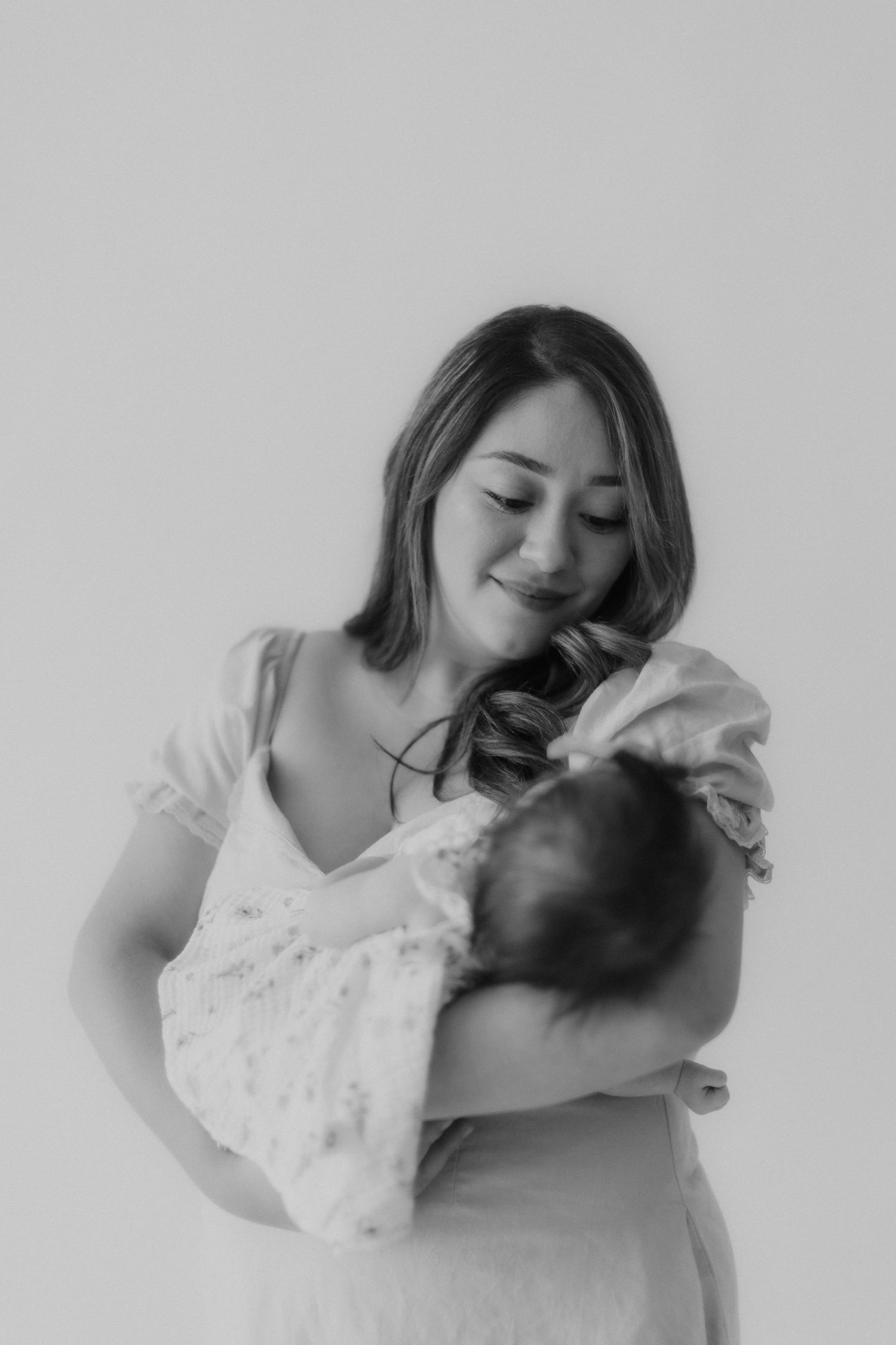 Black and white photo of a smiling mother in a white dress tenderly cradling her newborn baby.