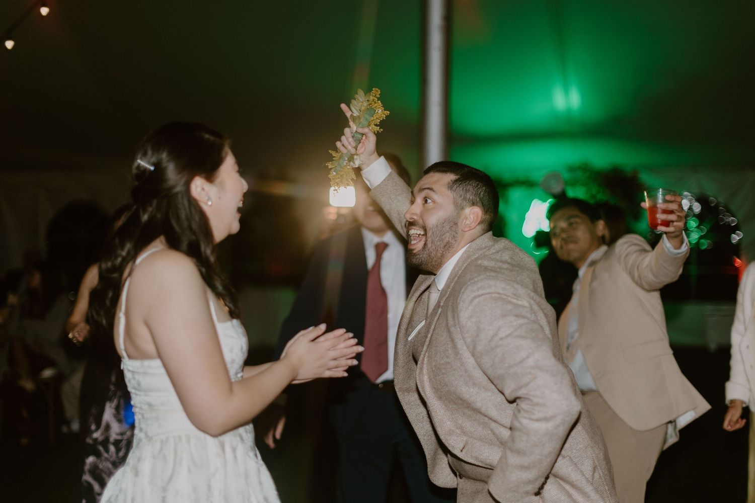 Bride and groom celebrating joyfully on wedding dance floor under green lights.