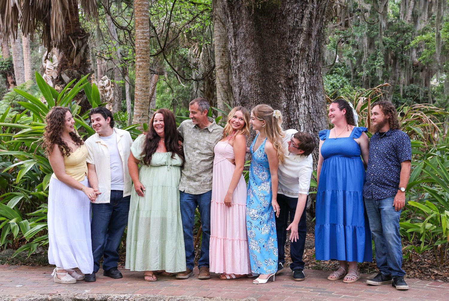A large family group poses outdoors among lush tropical greenery and trees, wearing pastel attire at Washington Oaks State Park in Florida.