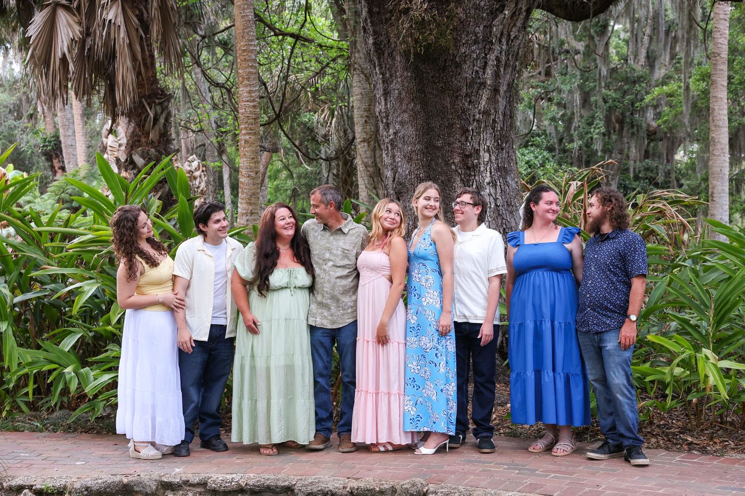 Large family group posing together outdoors in a lush tropical garden setting with tall trees.