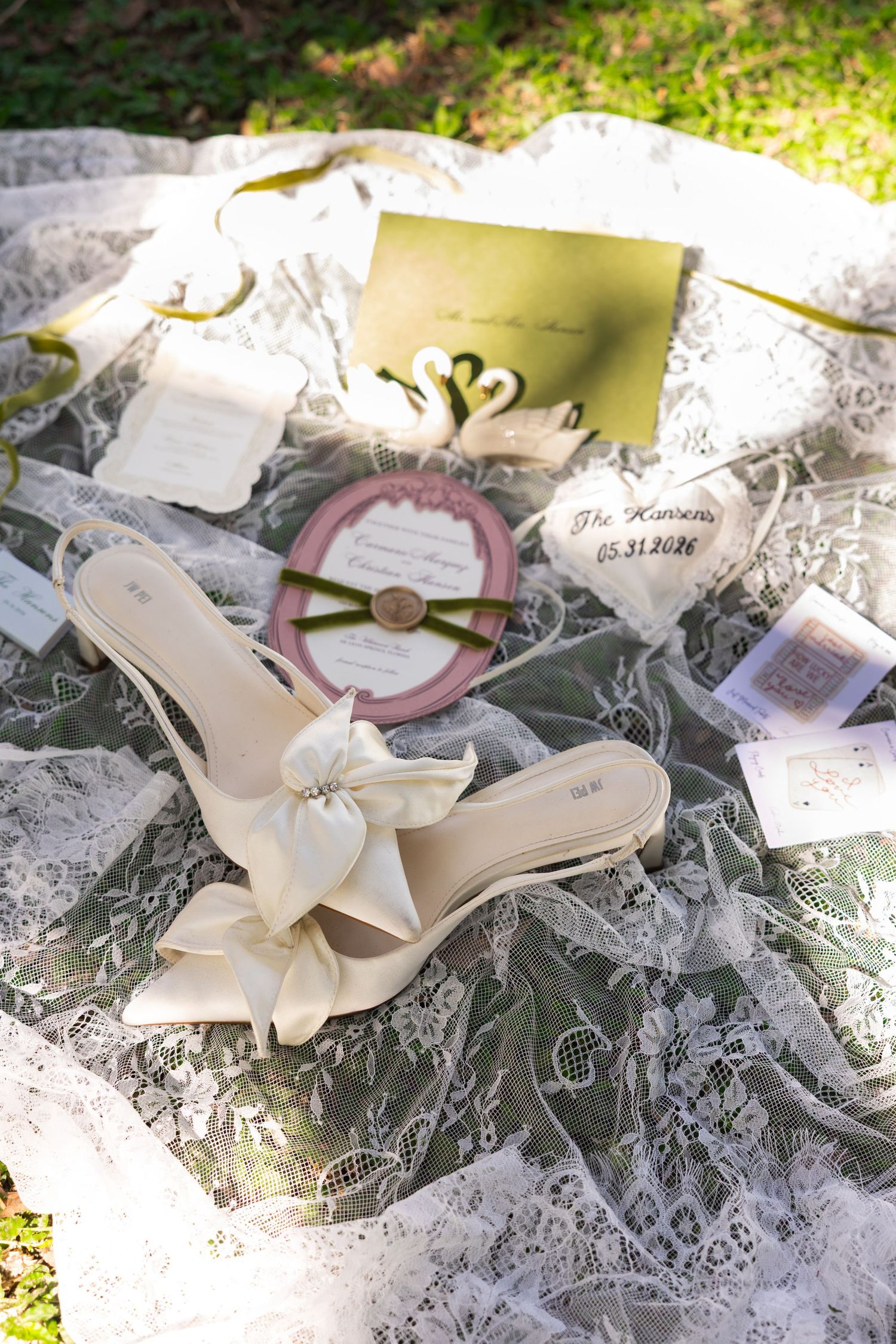 Elegant bridal flat sandals with bow detail on lace fabric surrounded by wedding stationery and accessories.