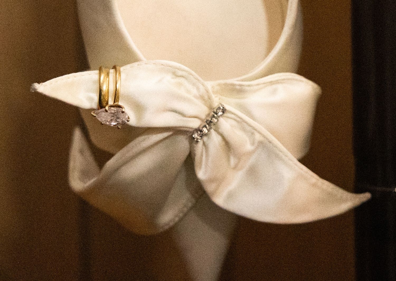 White satin bridal shoe with rhinestone bow detail and gold wedding rings displayed elegantly.
