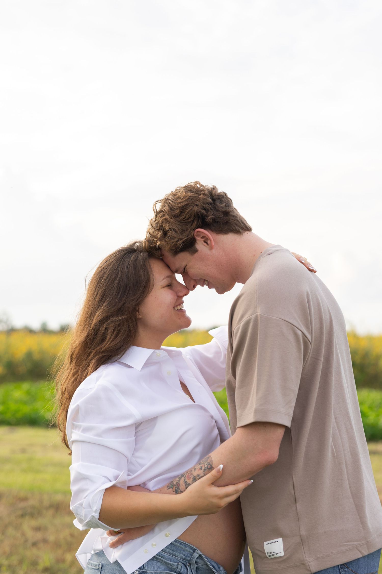 A young couple shares a romantic forehead-to-forehead moment outdoors, with the woman showing a pregnant belly.