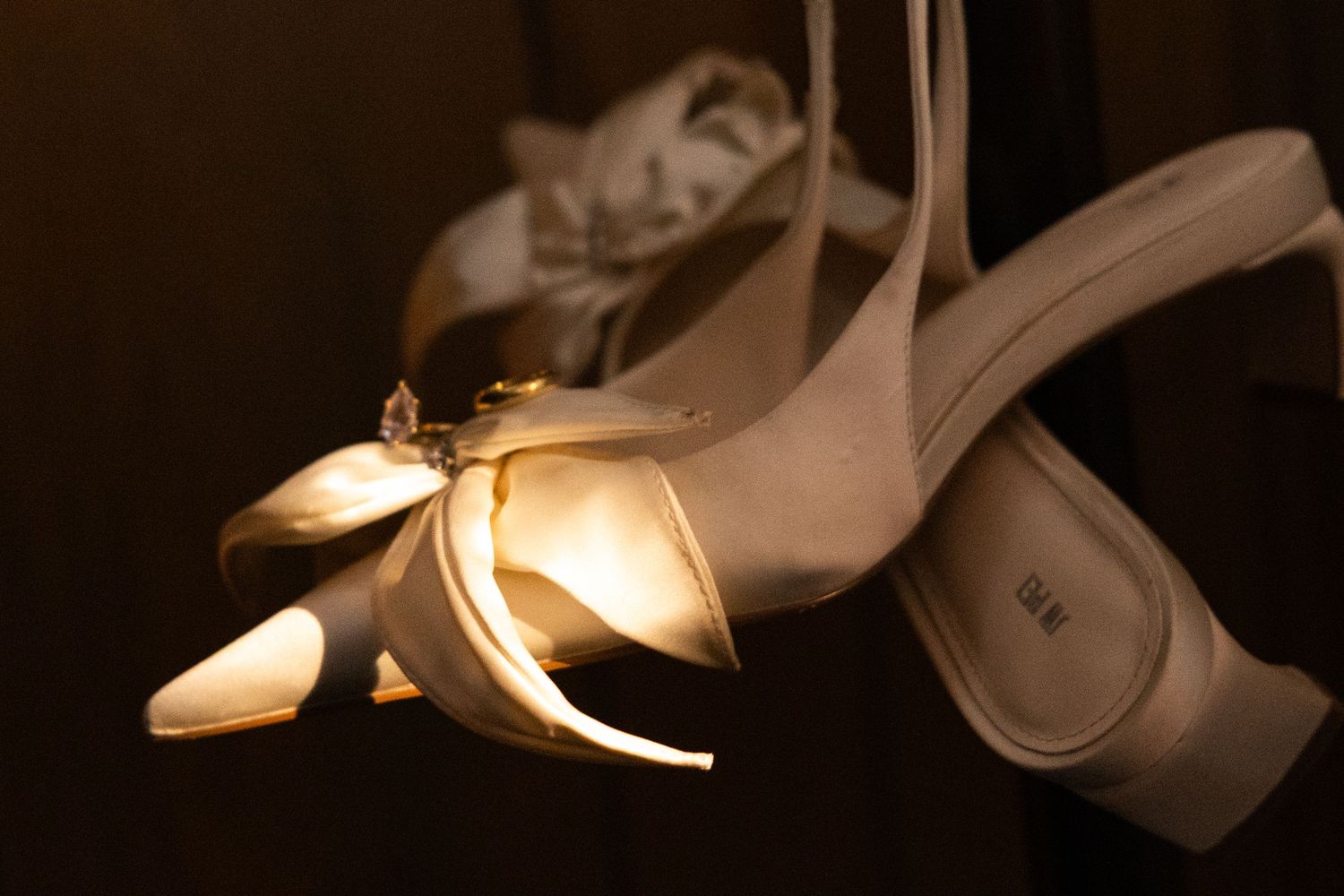 White bridal heels with satin bow detail displayed elegantly with soft warm lighting and wedding rings.