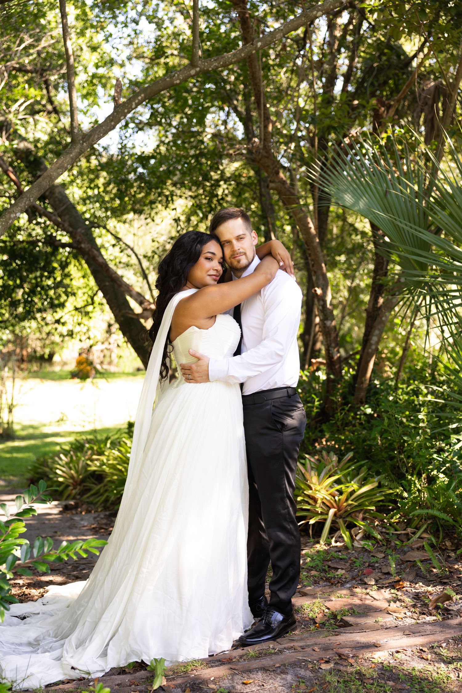 Bride and groom embracing outdoors in lush garden setting, wearing wedding dress and tuxedo.