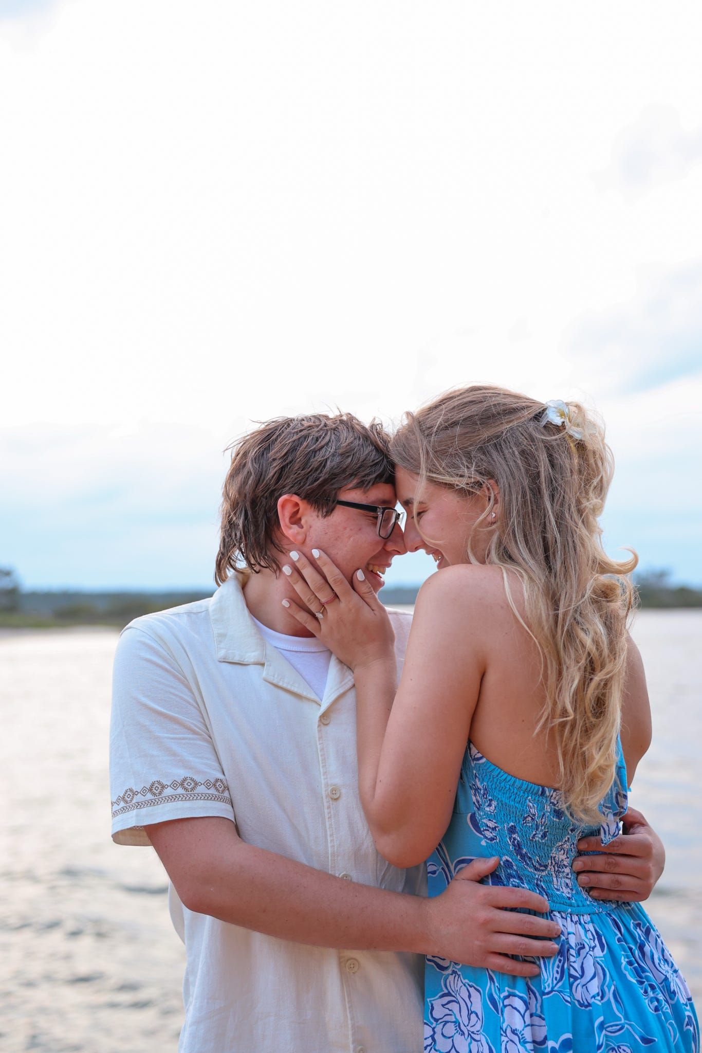 A romantic couple embracing and touching foreheads on a beach at dusk.