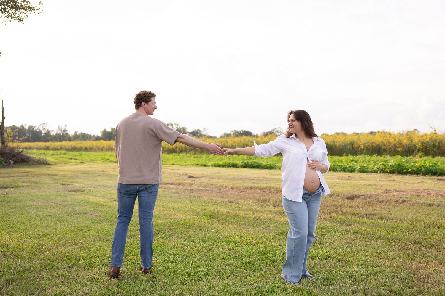 Couple holding hands and spinning together in a green field during an outdoor engagement photo session.