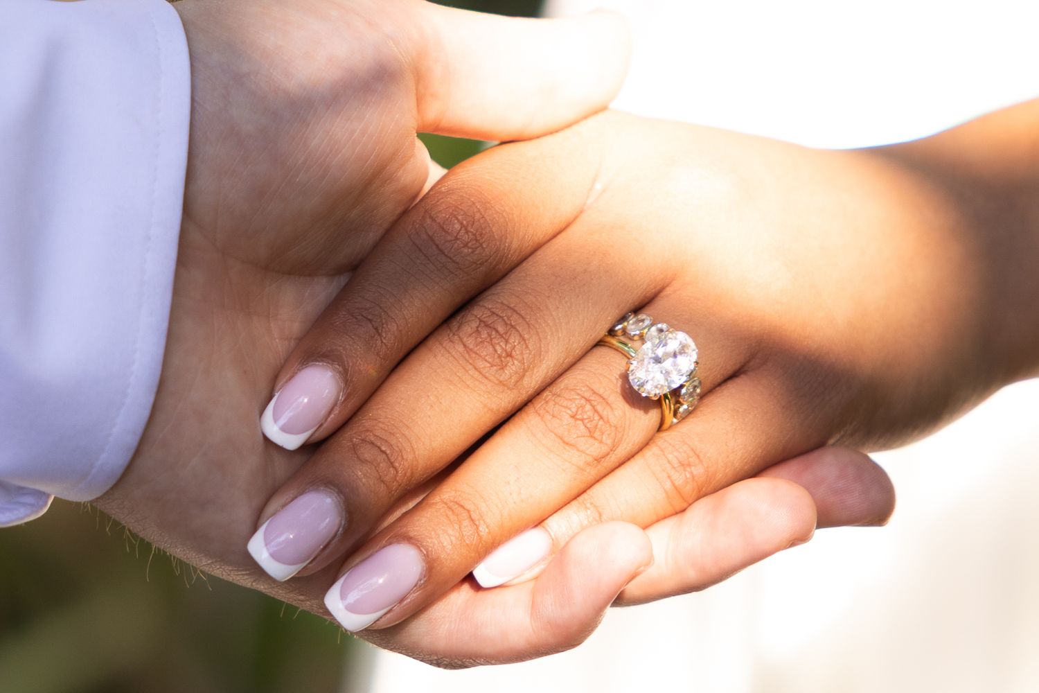 Close-up of hands holding, showcasing a stunning oval diamond engagement ring in a gold setting.