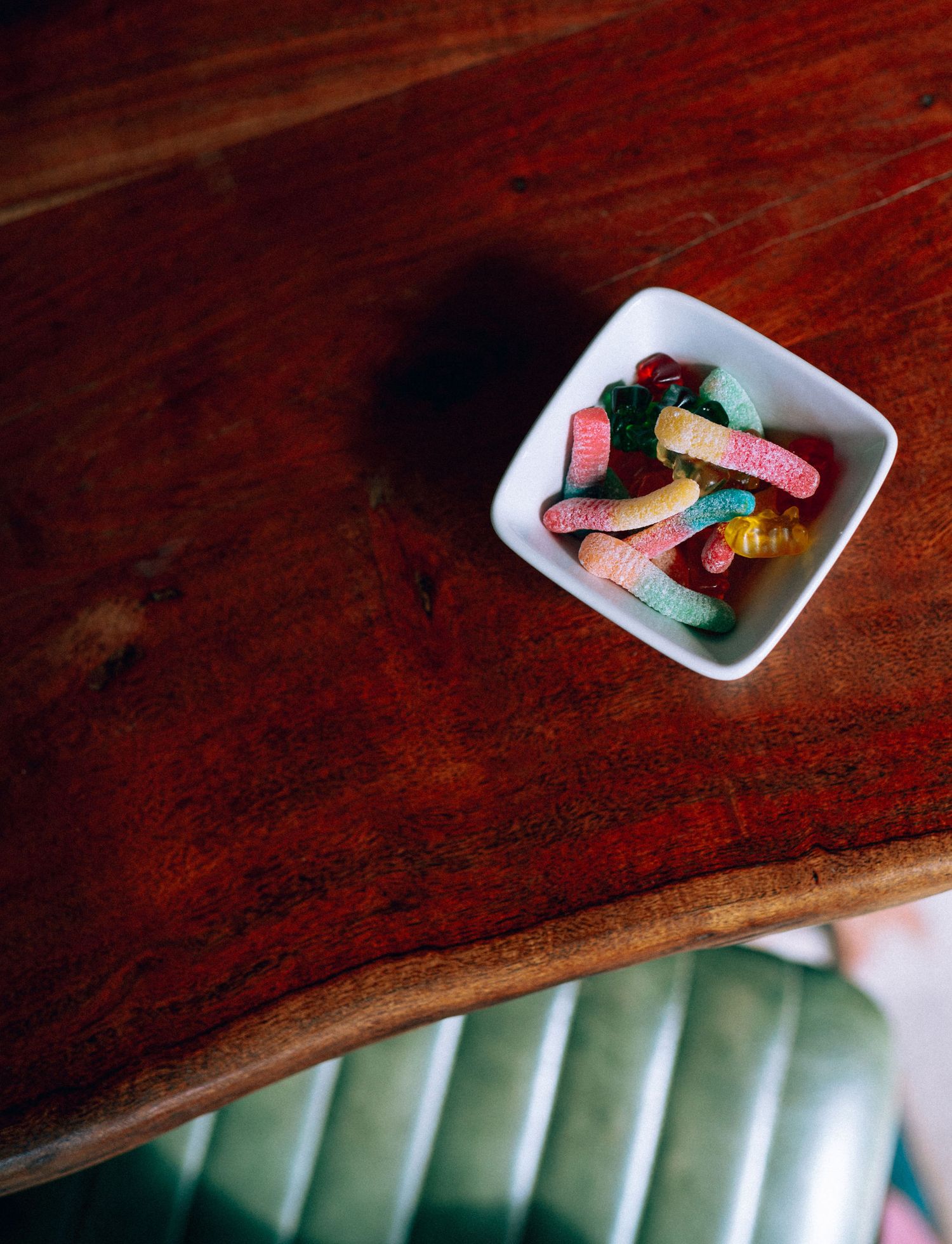 A white square bowl filled with colorful gummy worms and candies on a rustic wooden table.