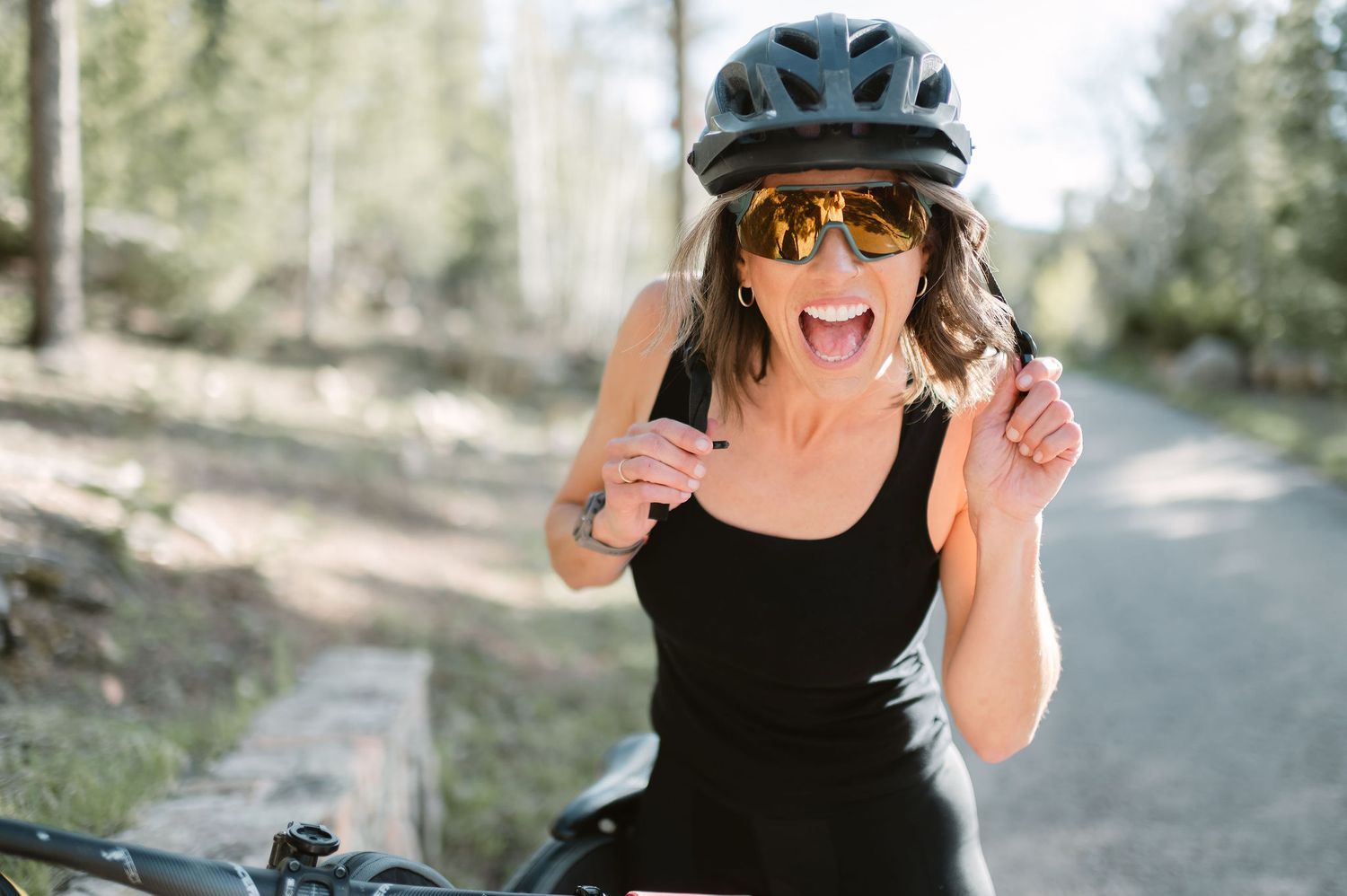 A cyclist in a black helmet and sunglasses poses for a series of expressive photos outdoors.