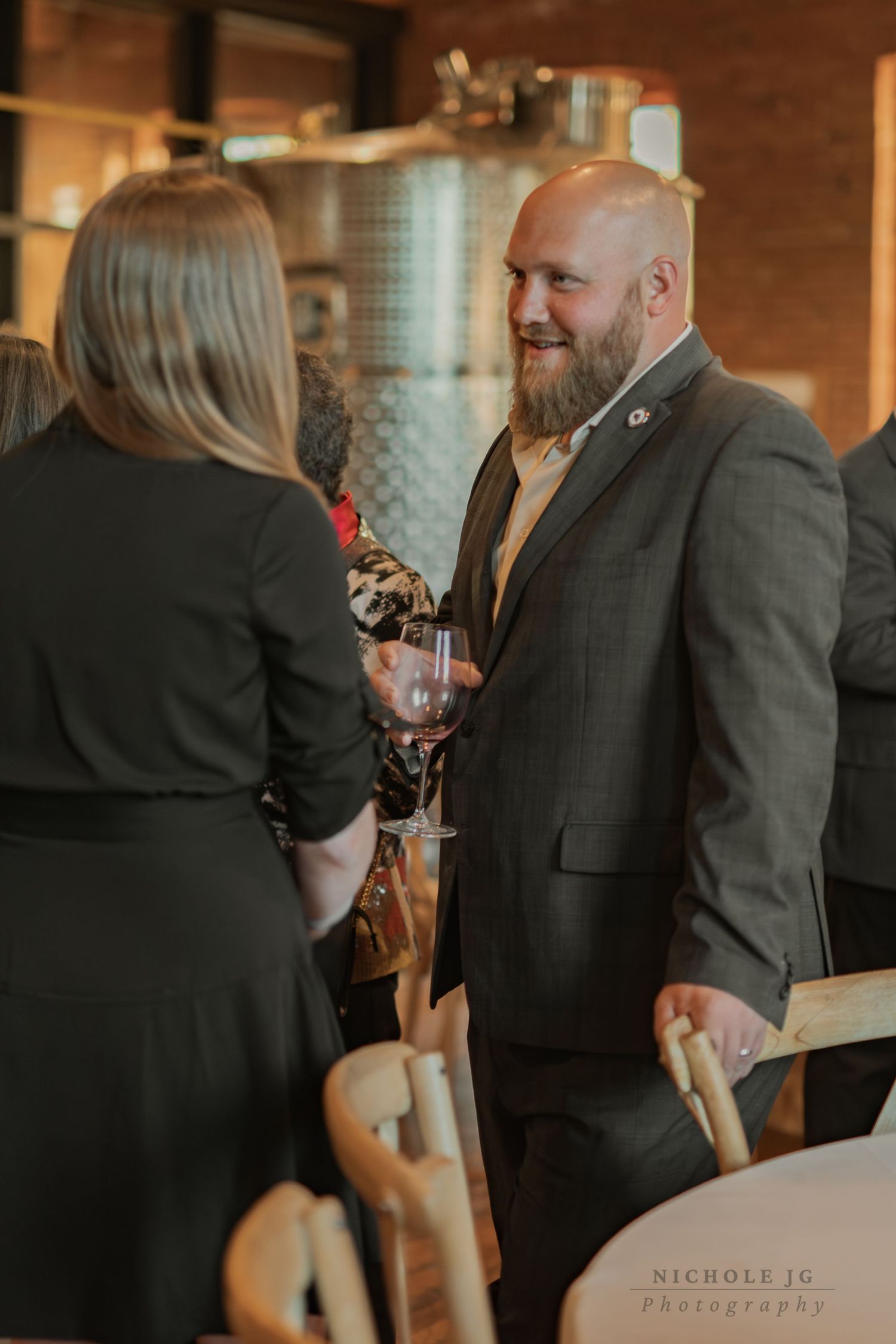 Bearded man in gray suit holding red wine glass chatting at elegant winery event with guests in background in the Hudson Valley