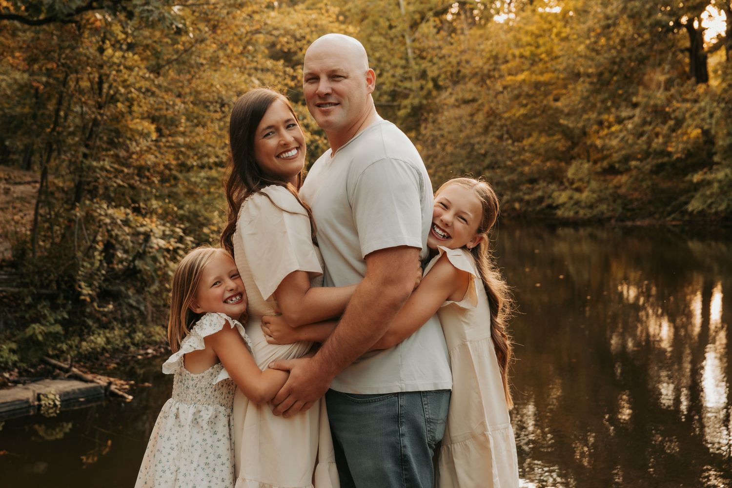 Happy family of four posing outdoors near a serene creek surrounded by lush autumn trees.