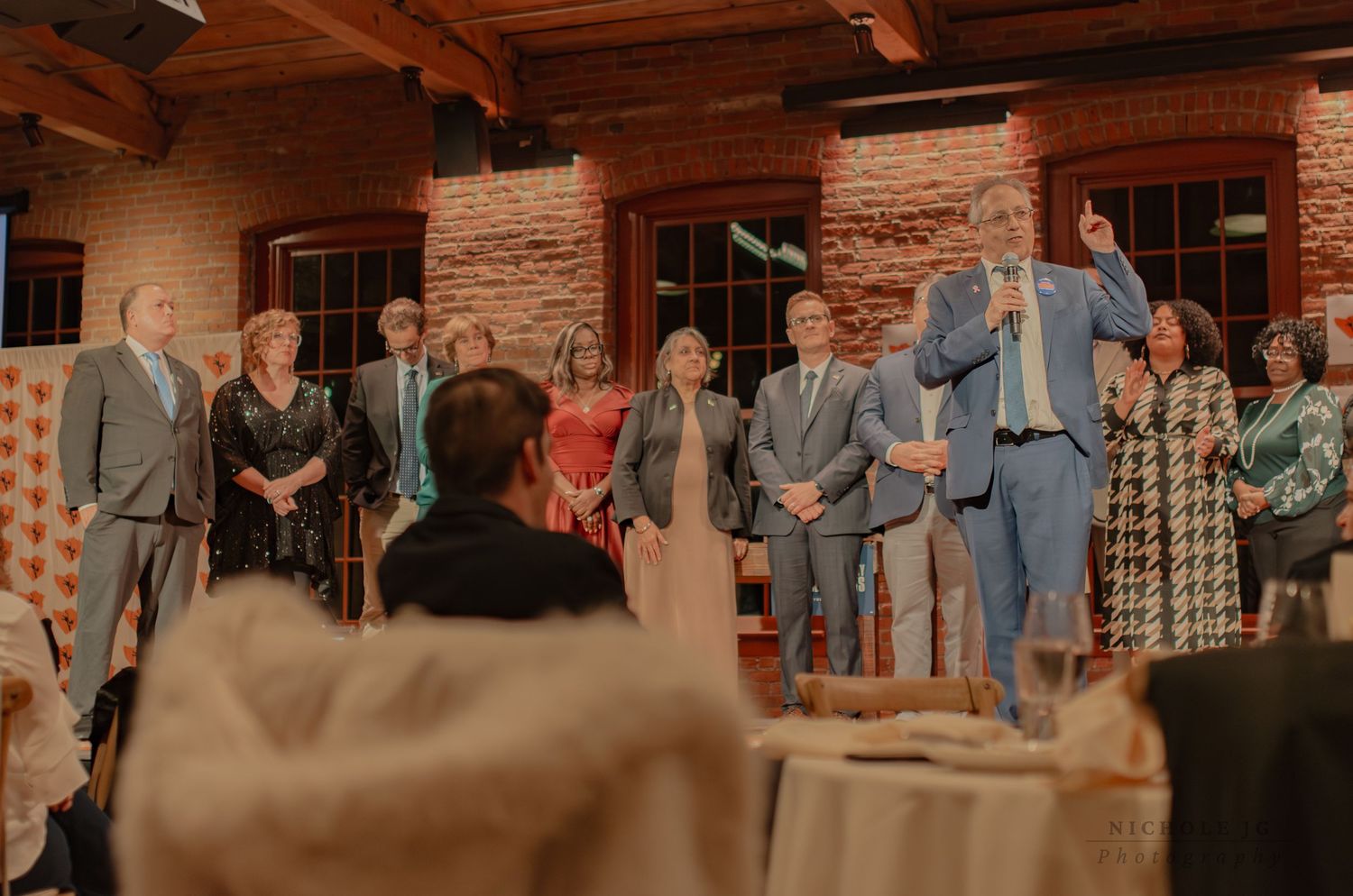 Elegant wedding reception speech in rustic brick venue with guests gathered around decorated tables.