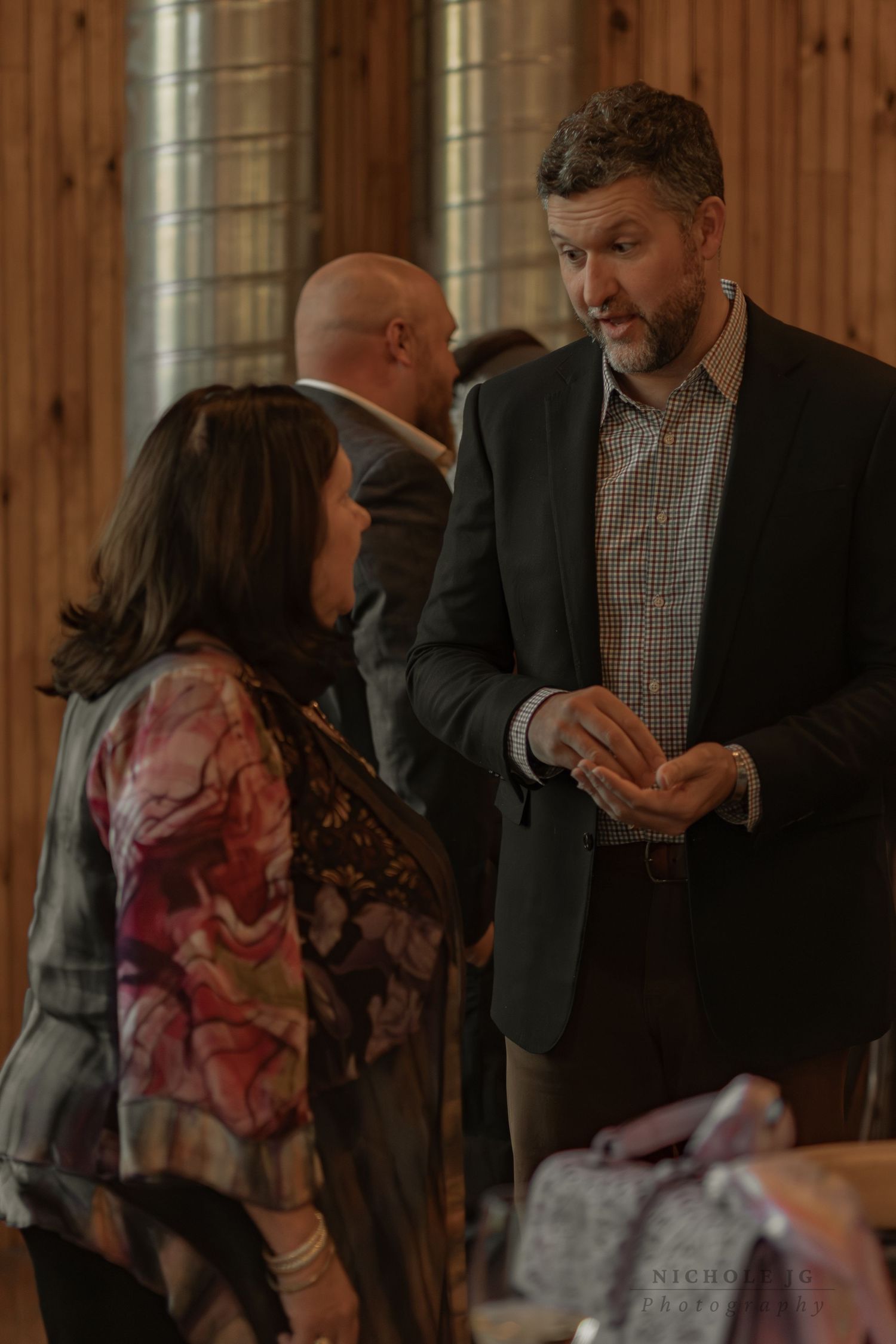 Two professionals engaged in conversation at an indoor event, man in blazer speaking with woman in floral top.