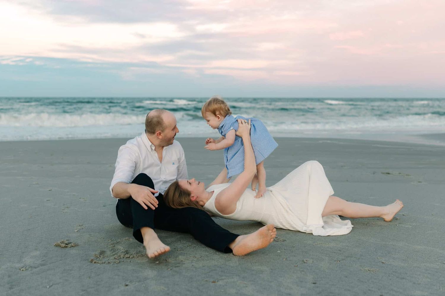 Family Ponte vedra beach photo at sunset with parents playing with toddler on sandy shore near ocean waves.