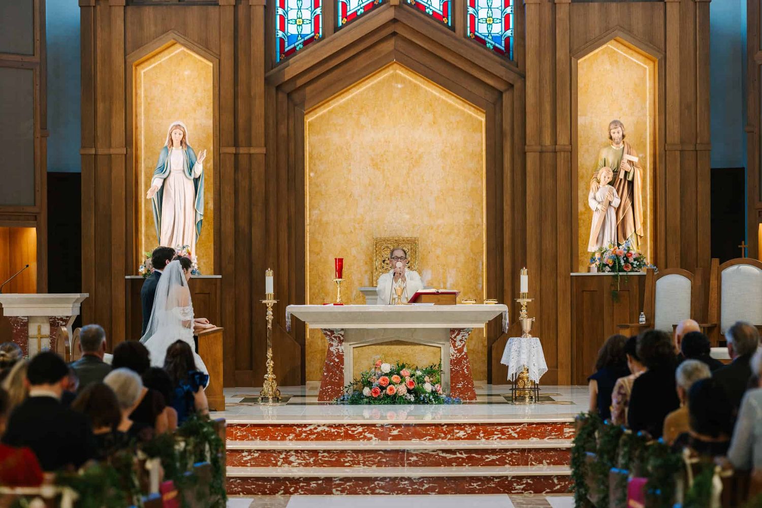 bride and groom kneeling on the left as priest is behind the altar for wedding
