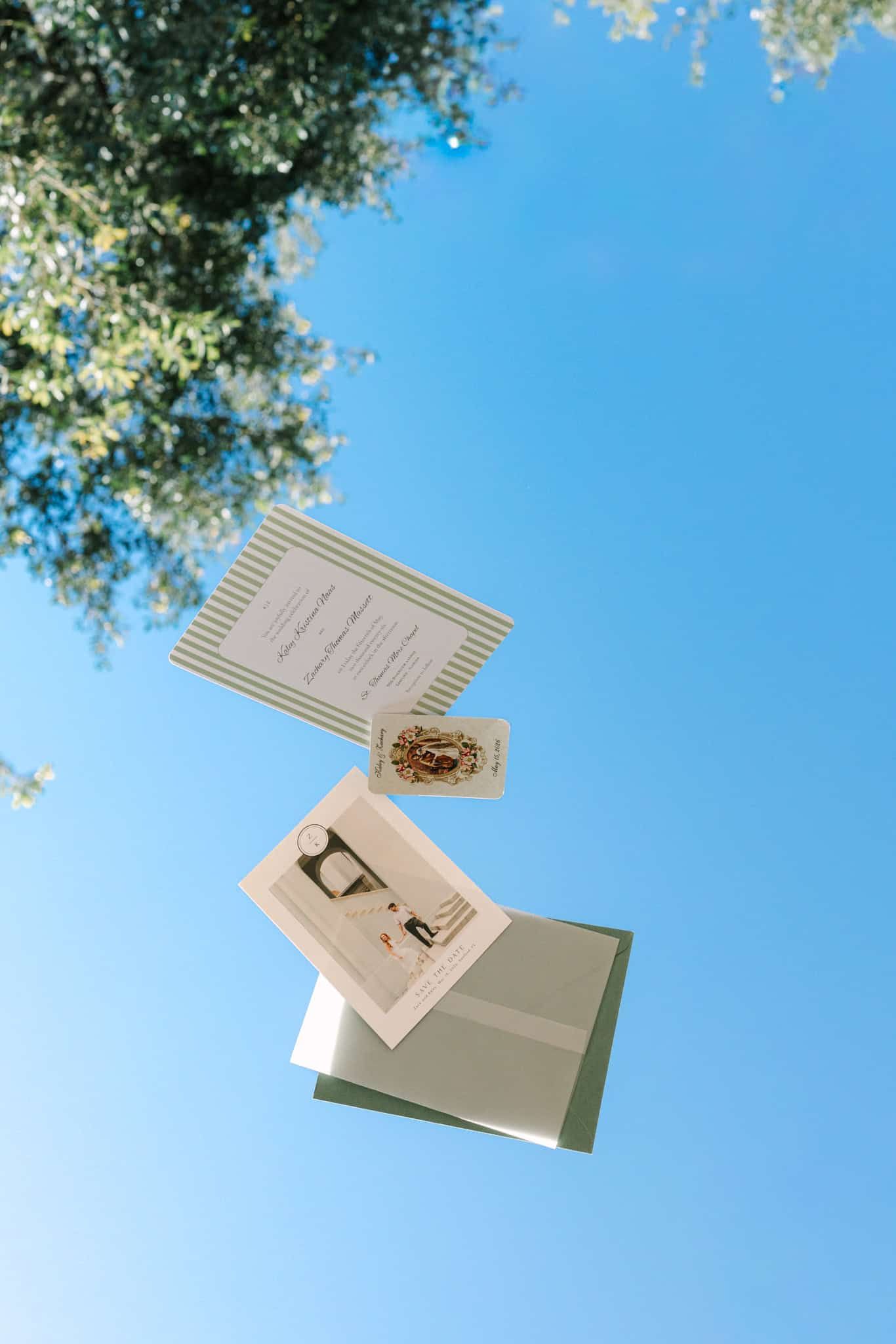 Wedding stationery suite floating against a clear blue sky with green tree foliage in the corner.