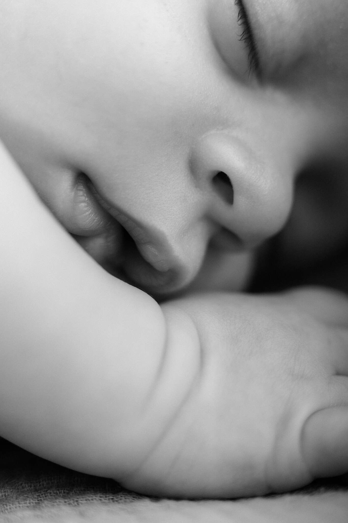 Black and white close-up portrait of a sleeping newborn baby with tiny hands near his face